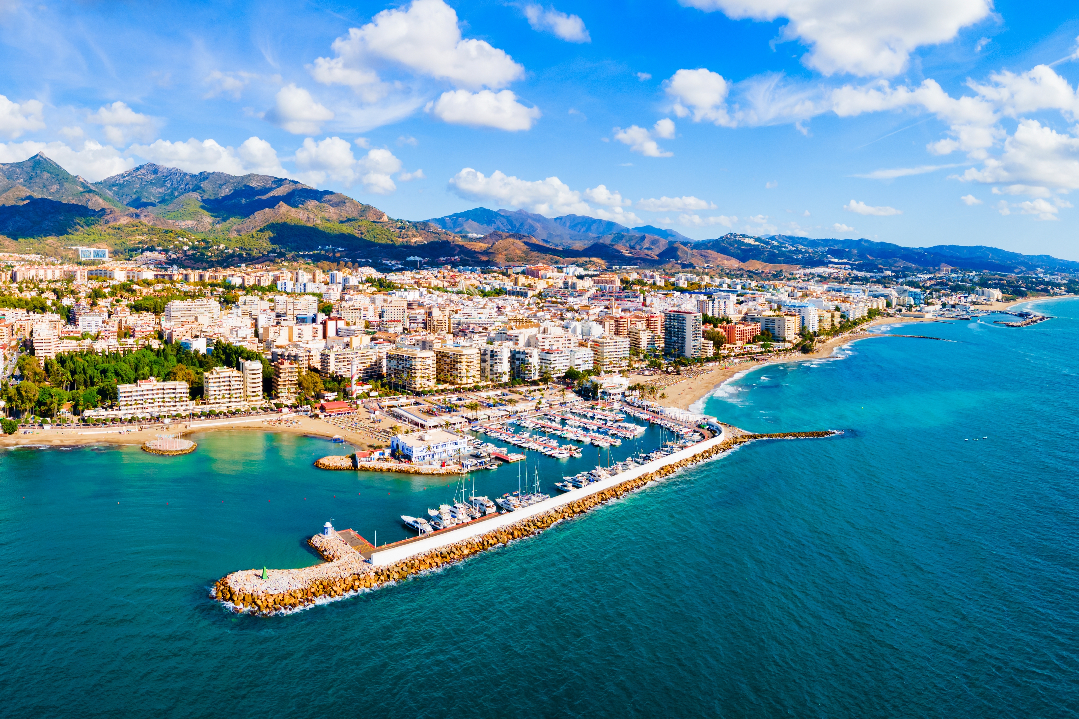 Smukt luftfoto af Marbella med marina, turkist Middelhav og bjerge i baggrunden på Costa del Sol, Spanien