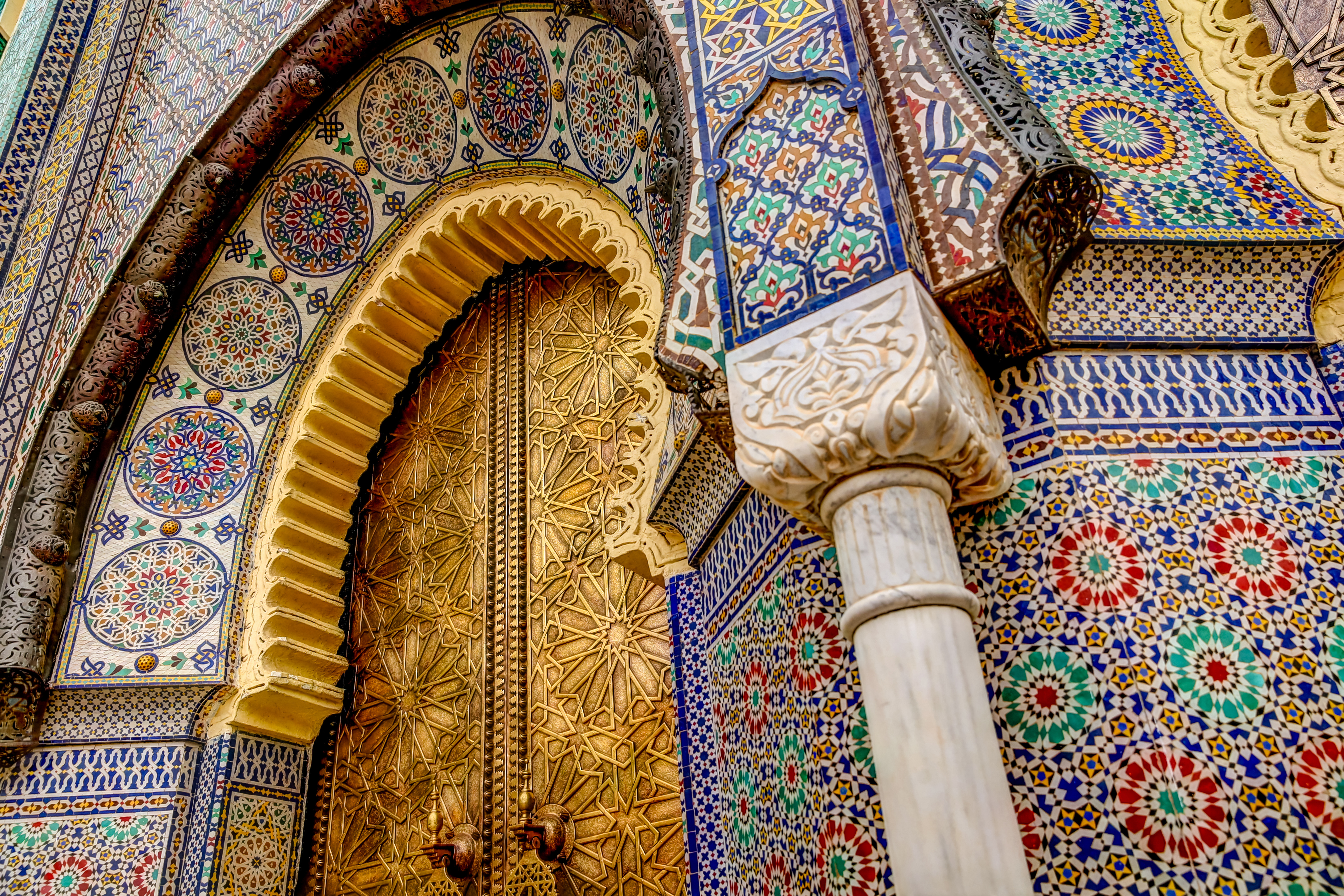 Farverige mosaikfliser og forgyldt portbue med traditionelle islamiske ornamenter ved kongepaladset i Fez, Marokko