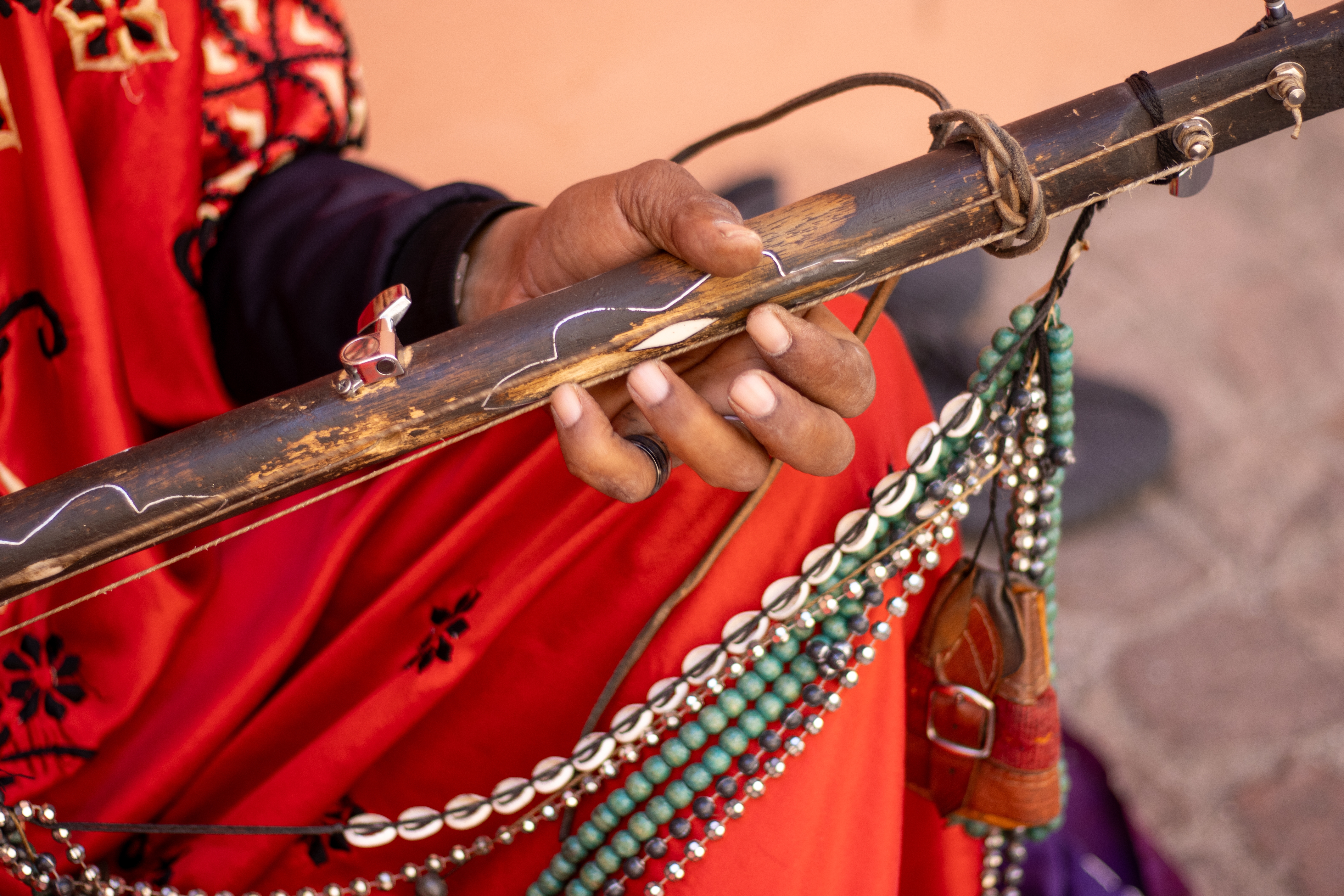 Nærbillede af hænder der holder et traditionelt Gnawa-instrument med perler og kauri-skaller i Marrakechs souk, Marokko