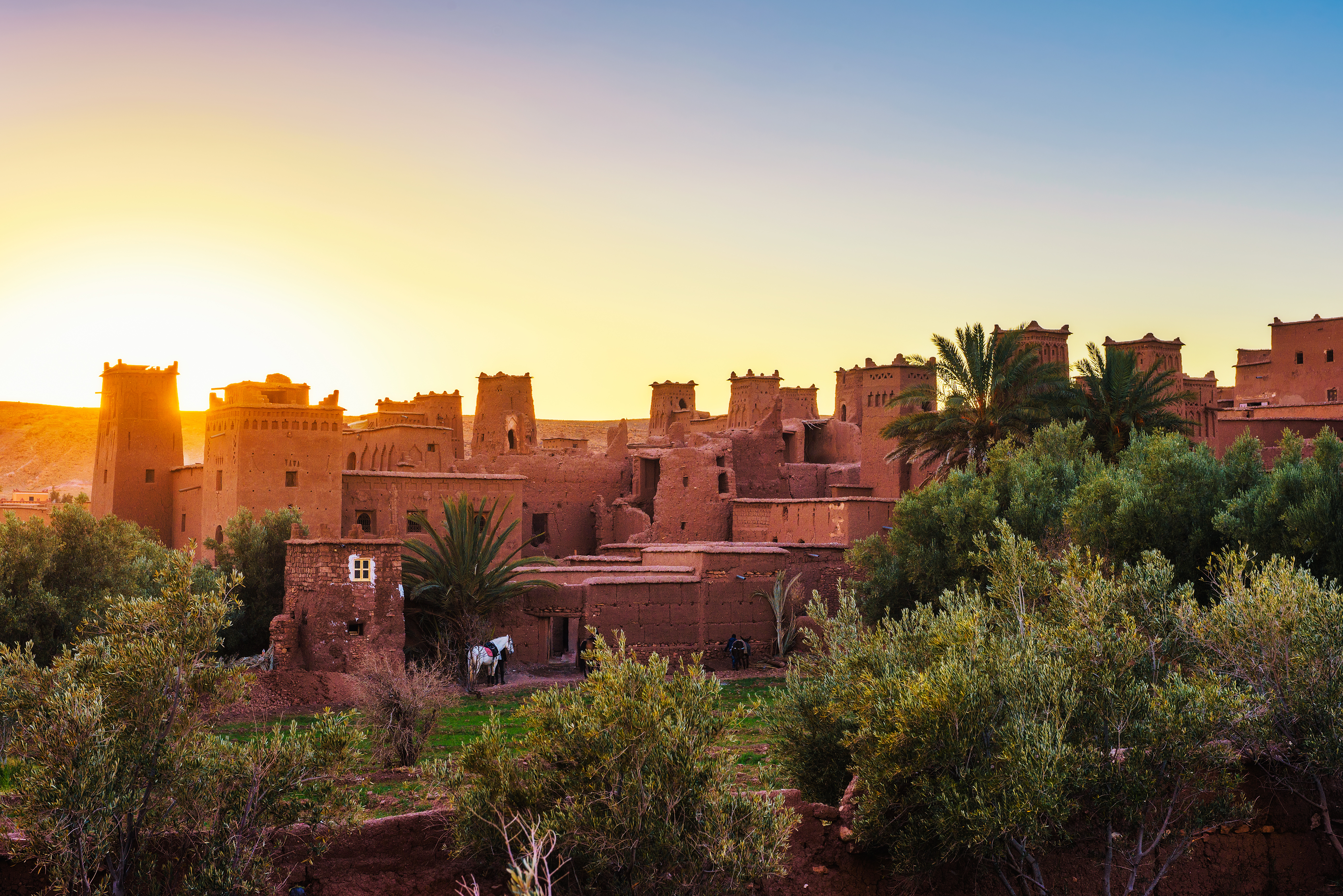Traditionel marokkansk kasbah i Ait Benhaddou ved solnedgang med berberarkitektur og palmer i forgrunden