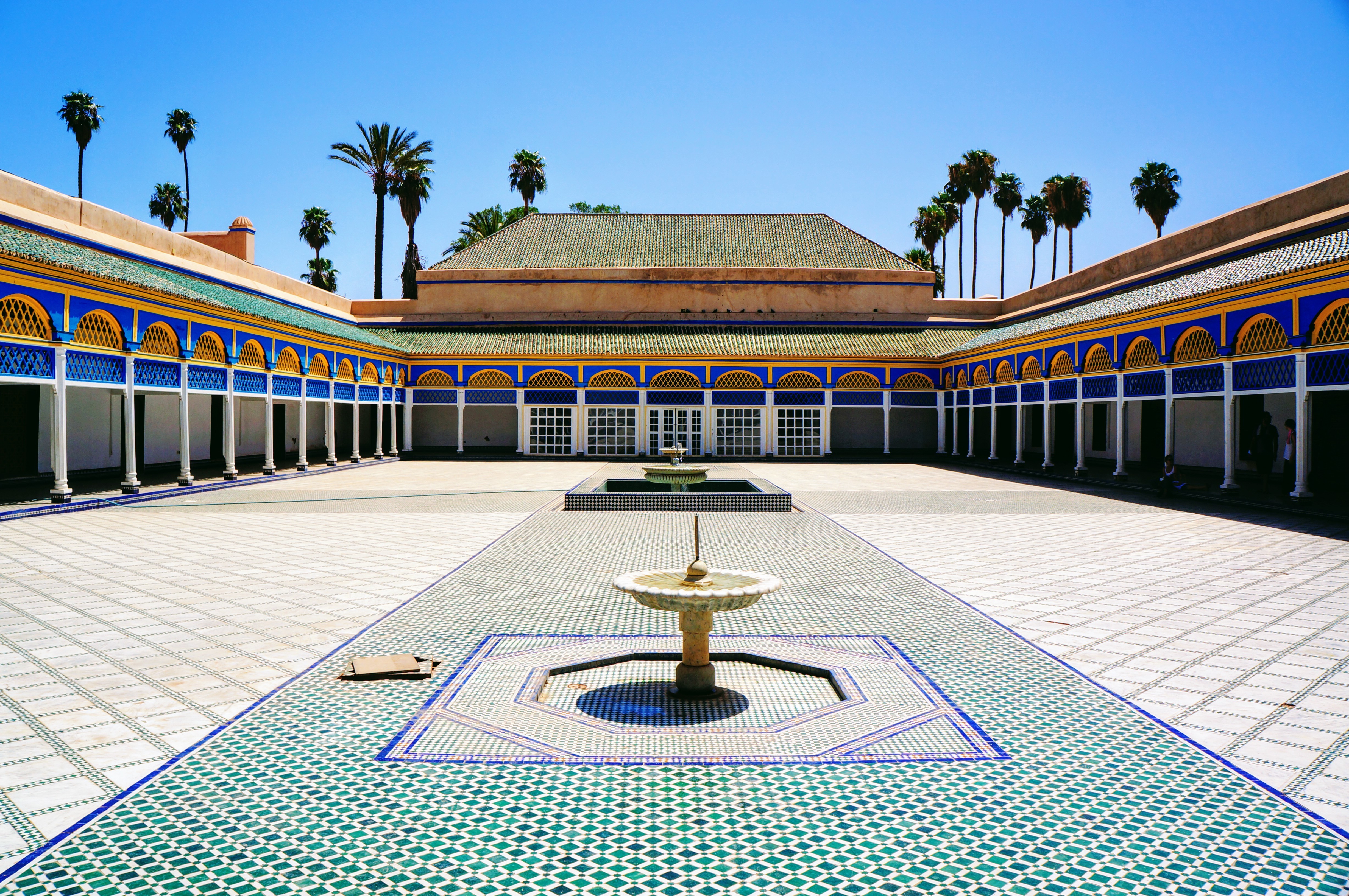 Udsigt over den indre gård i Bahia-paladset i Marrakech, Marokko, med flotte mosaikmønstre, klassiske hvide søjler og levende blå og gyldne udsmykninger
