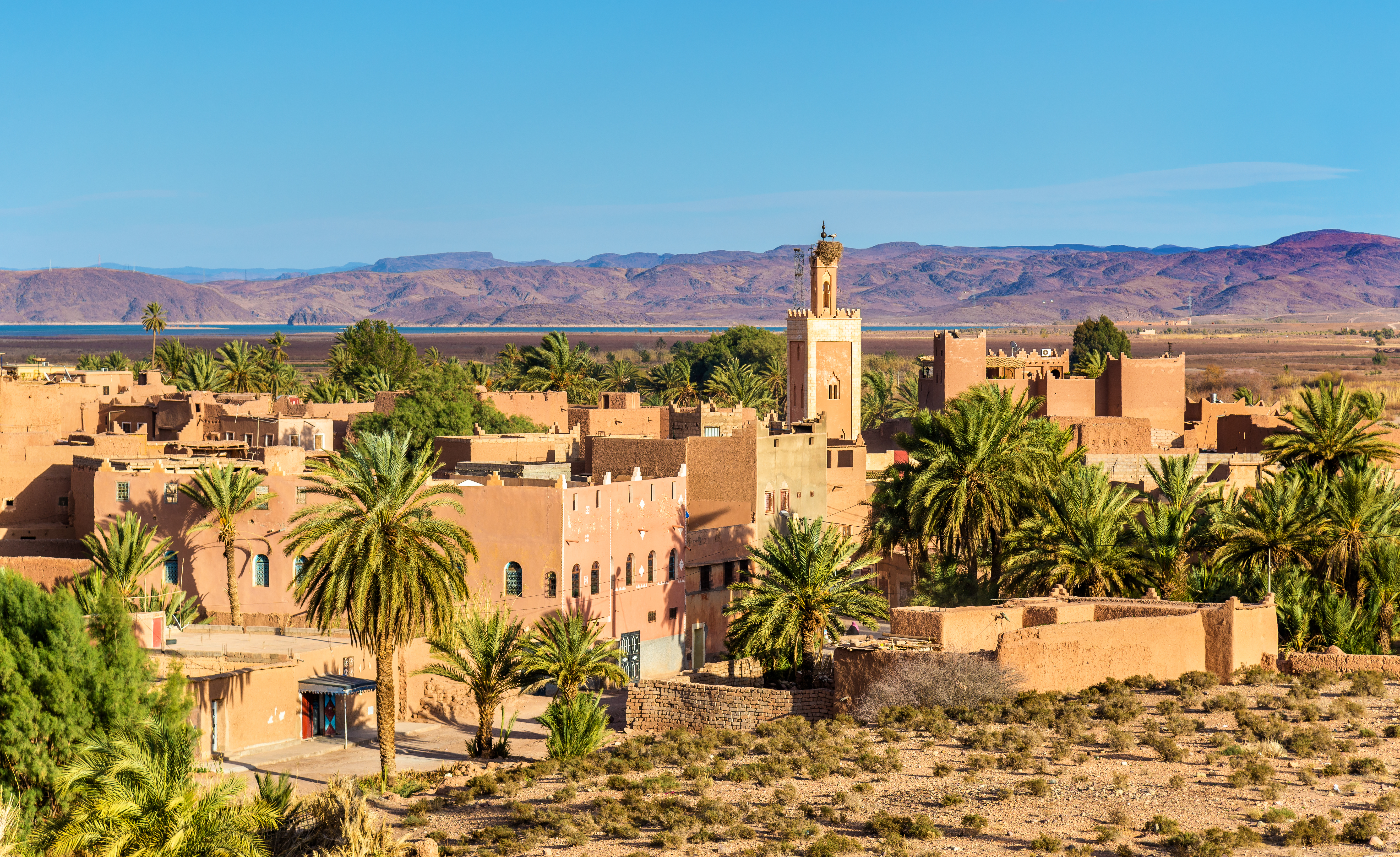 Traditionel marokkansk arkitektur i Ouarzazate med lerbyggede huse, en moské med minaret og frodige palmetræer omgivet af ørkenlandskab