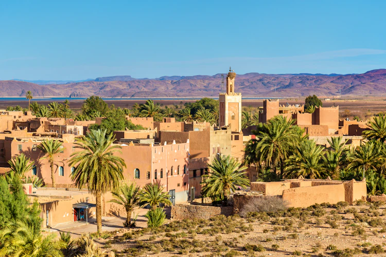 Traditionel marokkansk arkitektur i Ouarzazate med lerbyggede huse, en moské med minaret og frodige palmetræer omgivet af ørkenlandskab