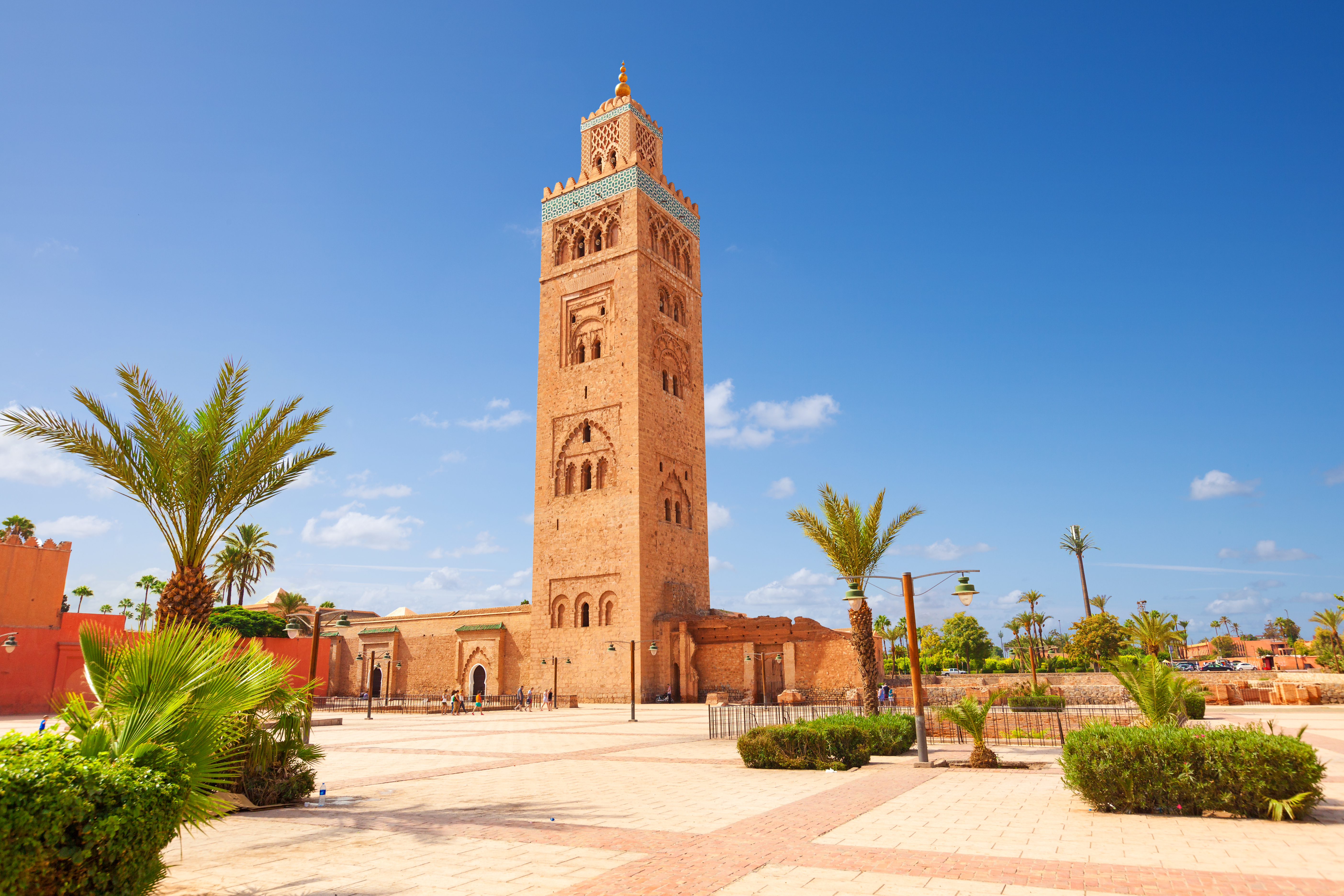Den ikoniske Koutoubia-moske i Marrakech, et af Marokkos mest fotograferede monumenter, med sin høje minaret der dominerer byens skyline, omgivet af frodige palmer og traditionel arkitektur