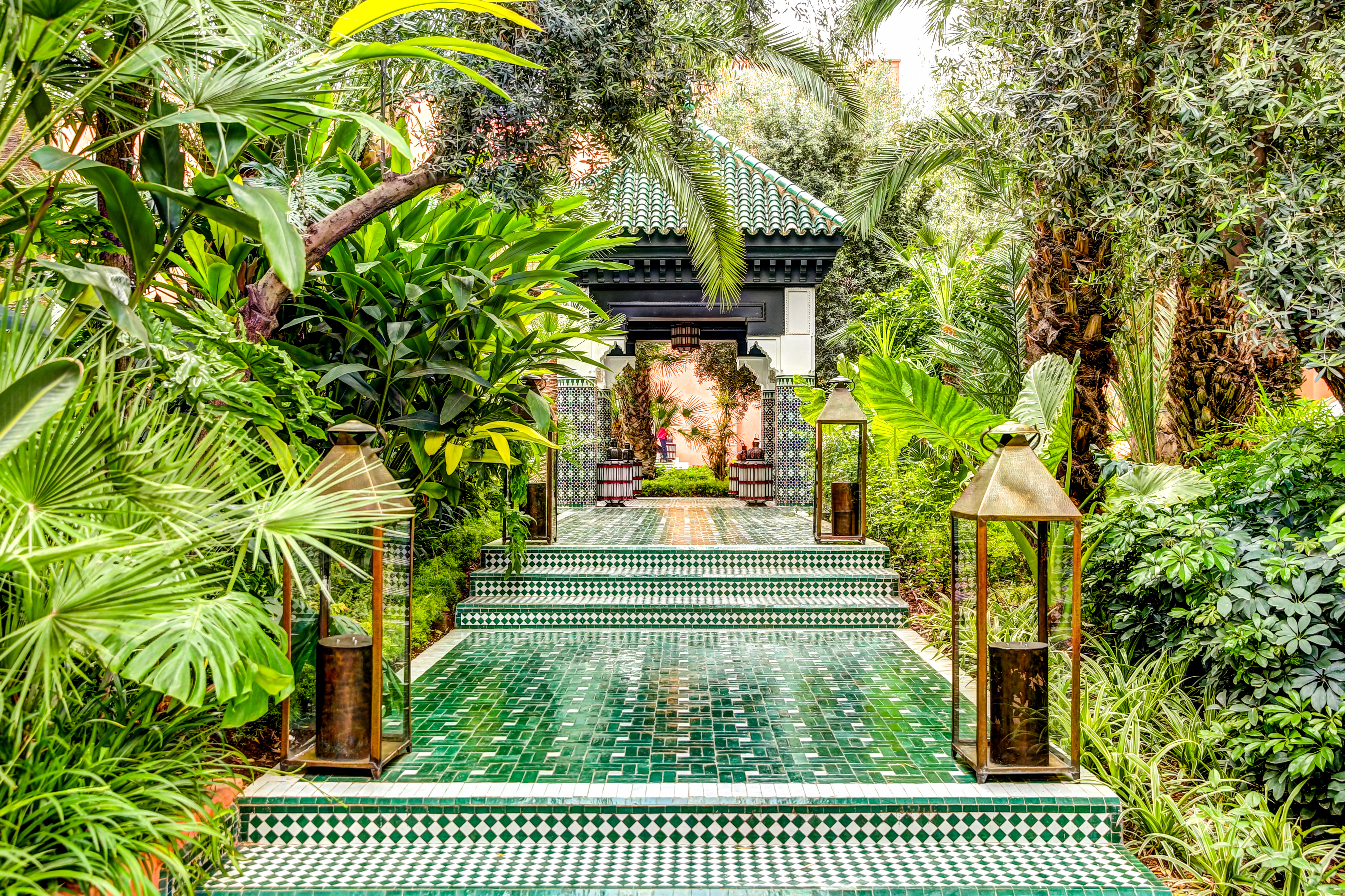 Smuk marokkansk have med grøn mosaiksti, messinglygter og palmer der leder mod en traditionel pavillon i Marrakech