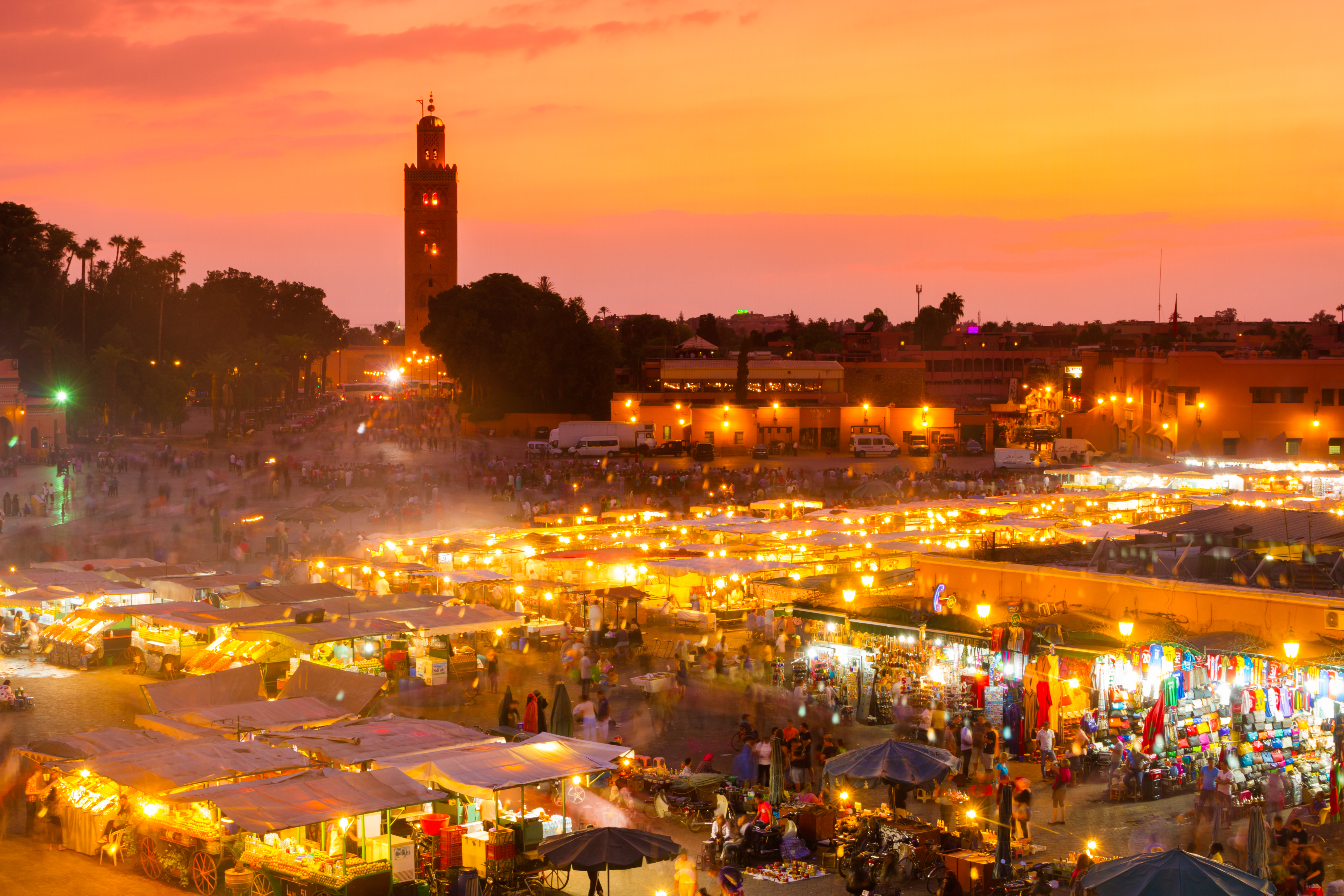 Panoramaudsigt over det livlige Jamaa el Fna torv i Marrakechs medinakvarter ved solnedgang med boder, gadehandlere og den historiske Koutoubia-moske i baggrunden