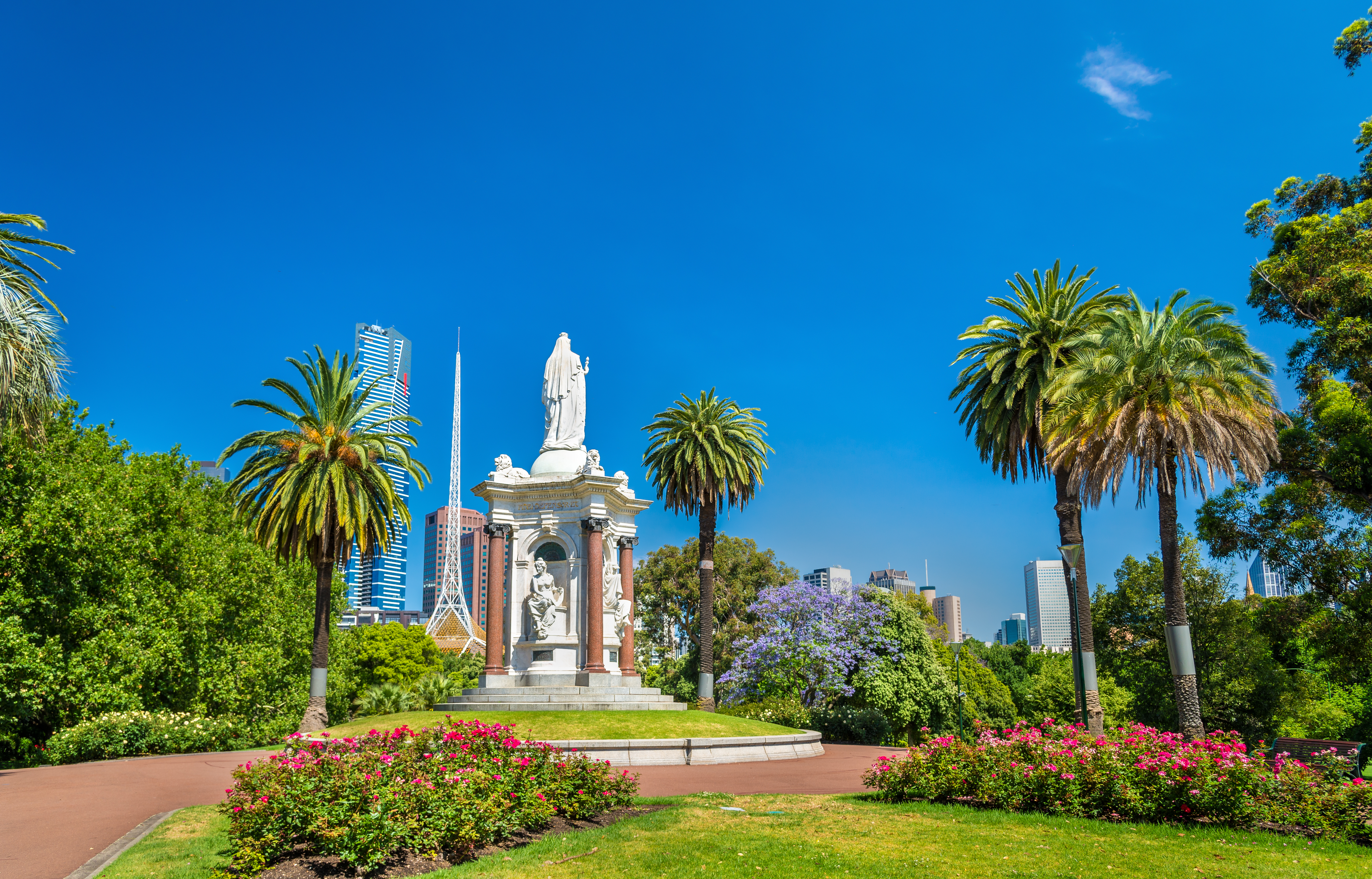 Victoria statue i smuk park i Melbourne Australien med skyline baggrund