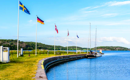 Göta Kanal ved Mem i Sverige med sejlbåde ved bryggen, nordiske flag og smuk skærgård i baggrunden på en solrig sommerdag