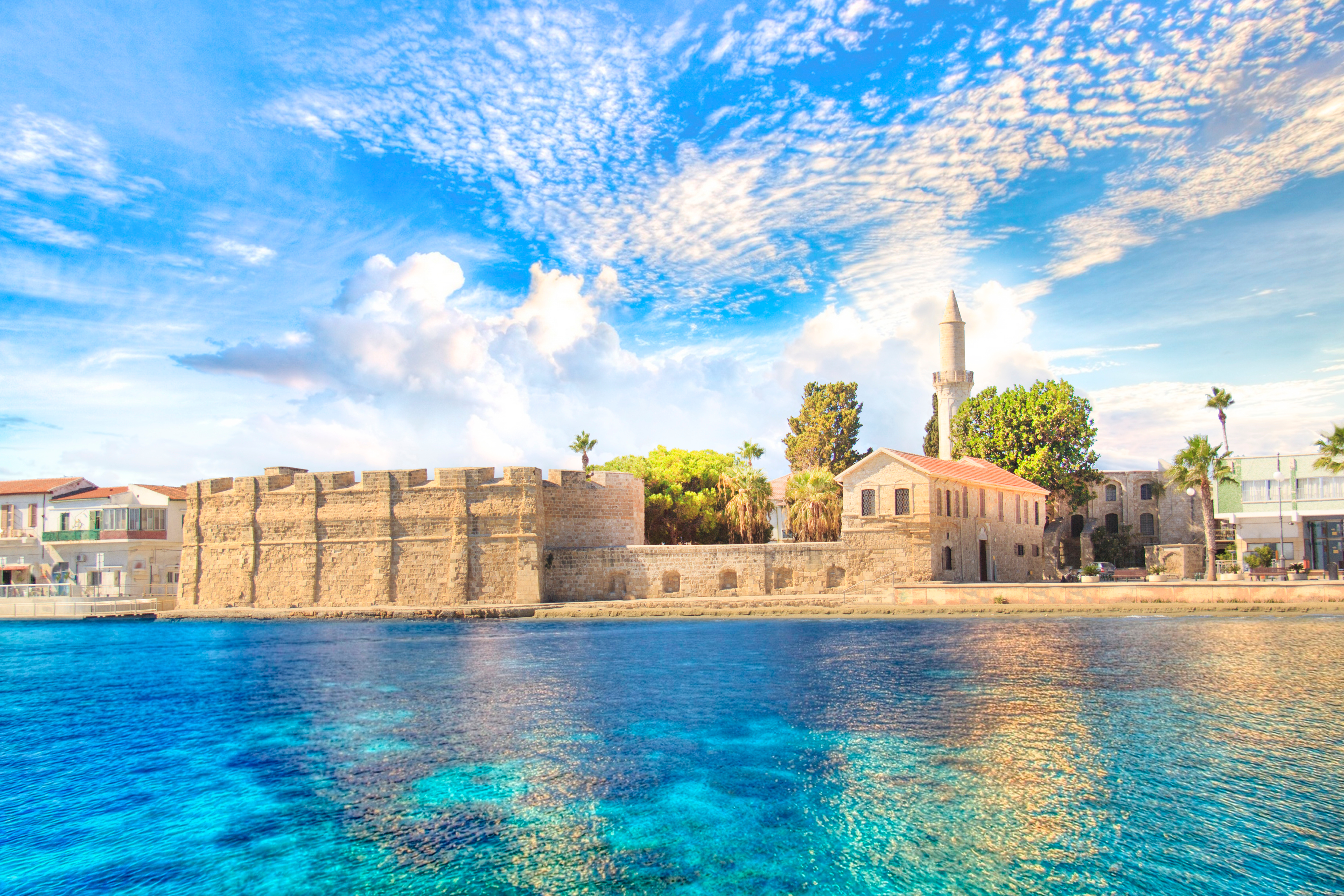 Middelalderslot ved Larnaca strand på Cypern med turkist vand og palmer under blå himmel