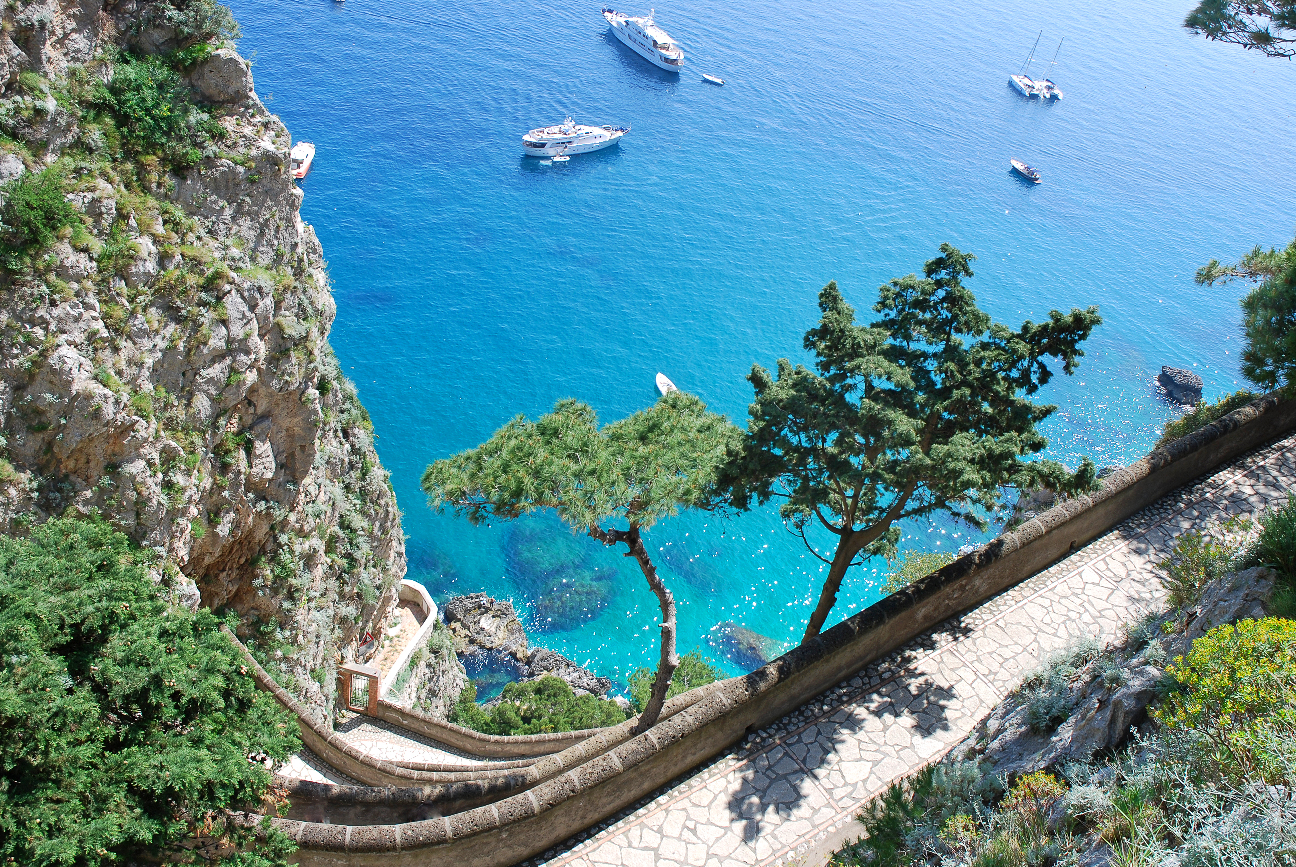 Idyllisk kystlandskab på Capri-øen nær Napoli med det azurblå Middelhav, grøn vegetation og snoede veje langs de dramatiske klipper