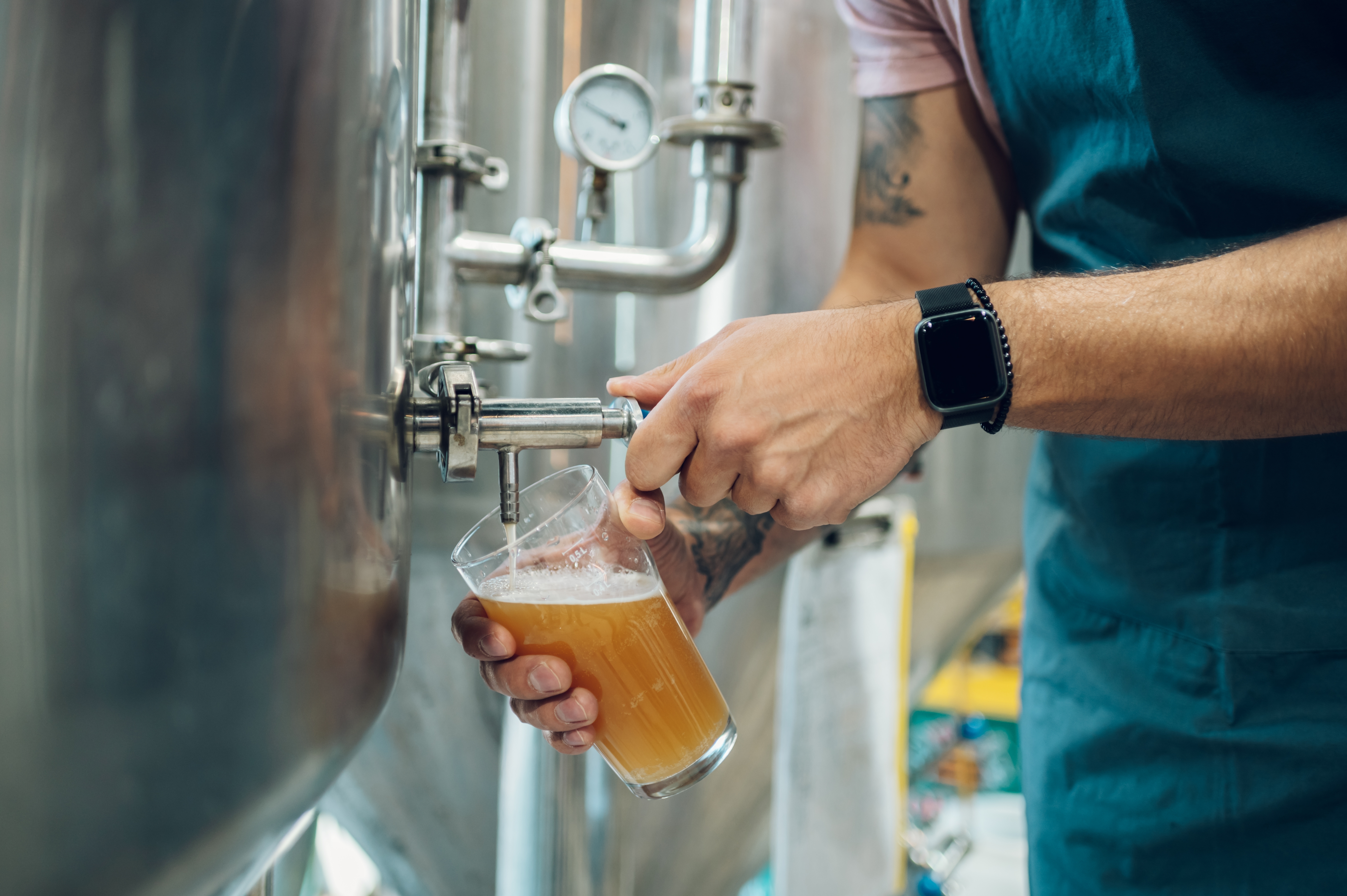 Brygmester kontrollerer ølkvalitet ved at tappe direkte fra fermentationstank i dansk mikrobryggeri
