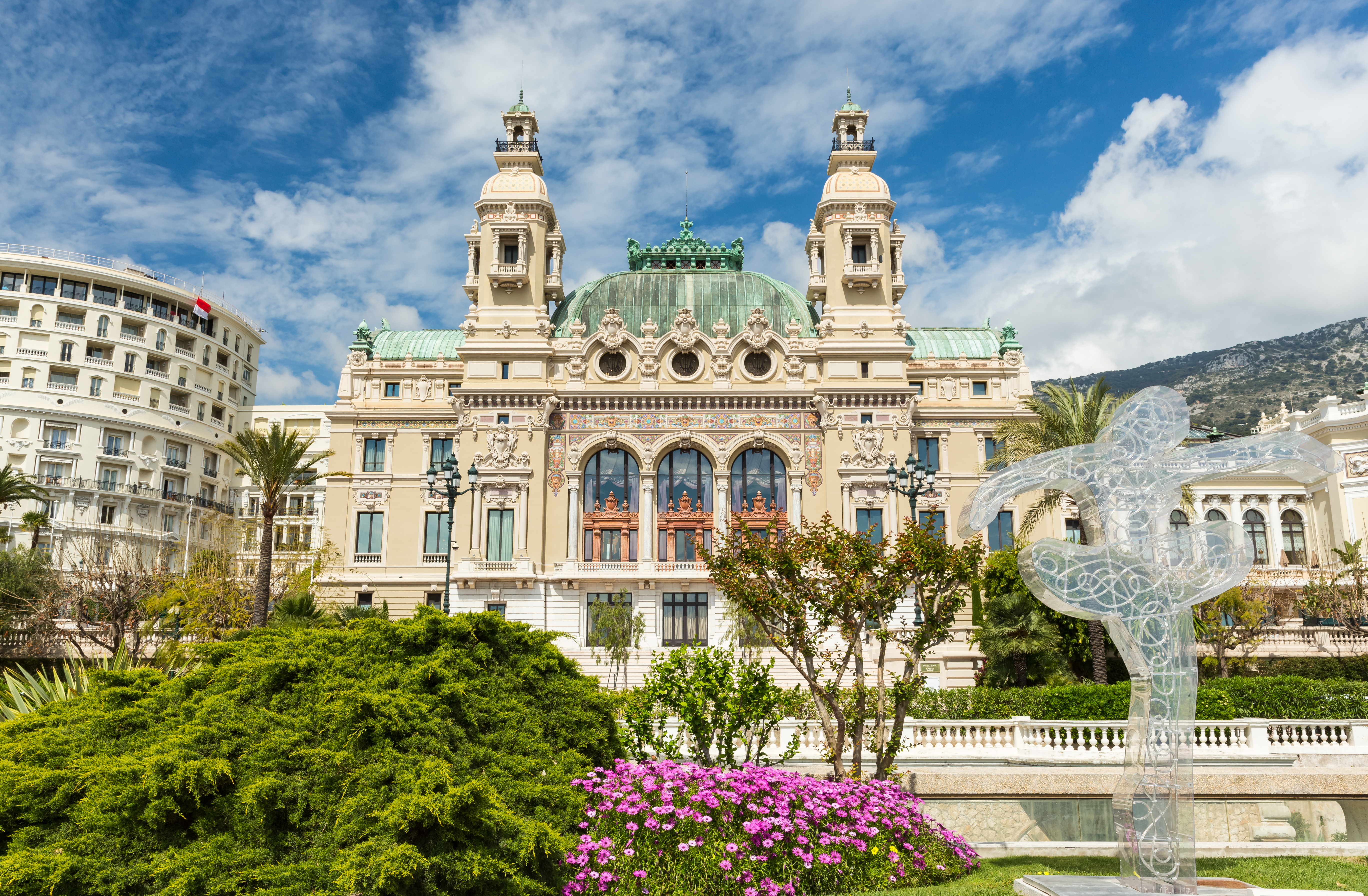 Det berømte Casino de Monte-Carlo i Monaco med overdådig arkitektur og smukke parkanlæg med farverige blomster under en blå himmel