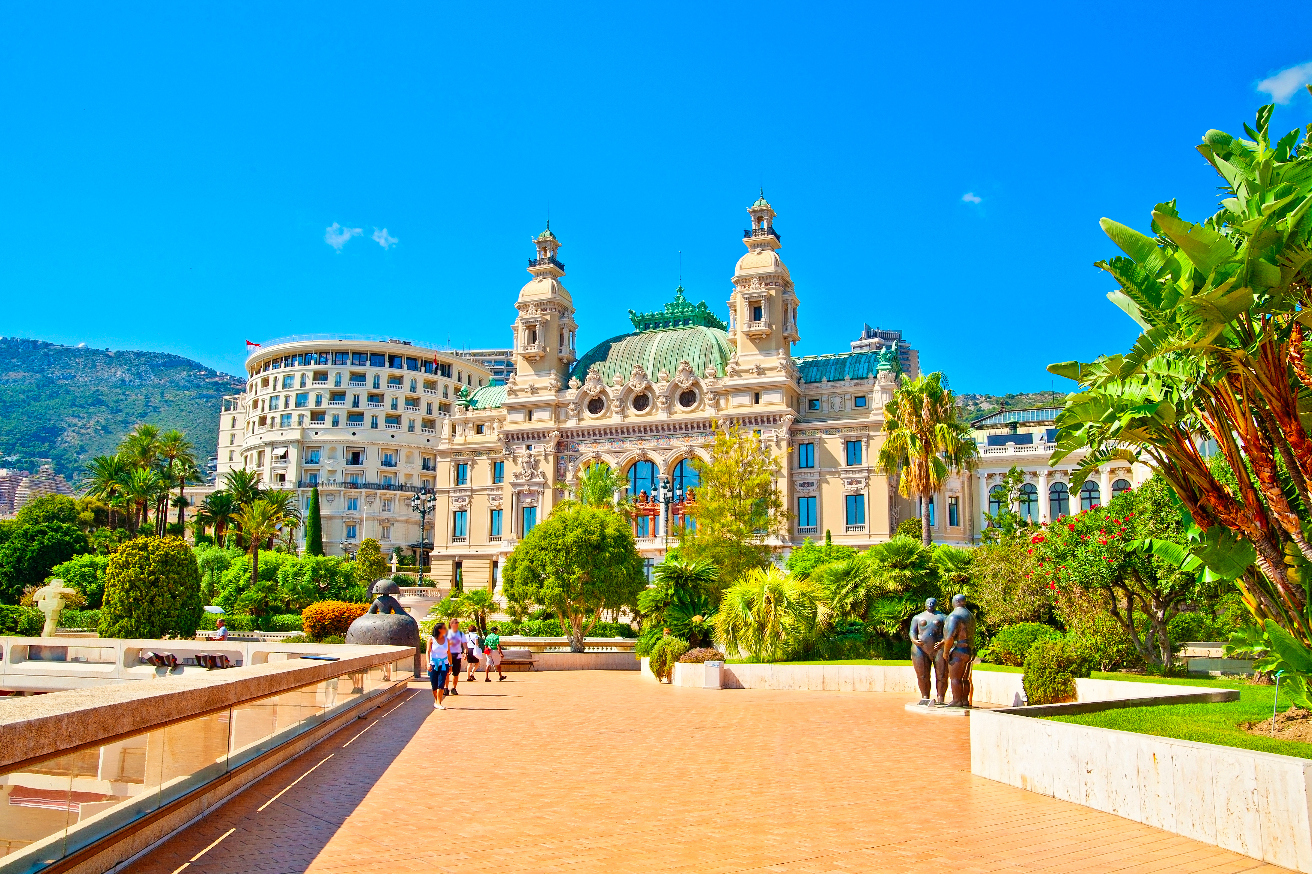 Sommerrejse til Monaco – det ikoniske Casino Monte-Carlo omgivet af grønne haver og palmer under blå himmel