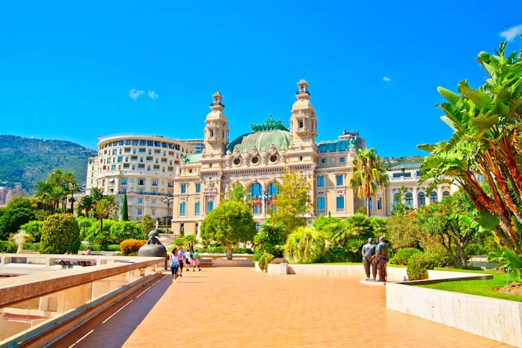 Sommerrejse til Monaco – det ikoniske Casino Monte-Carlo omgivet af grønne haver og palmer under blå himmel