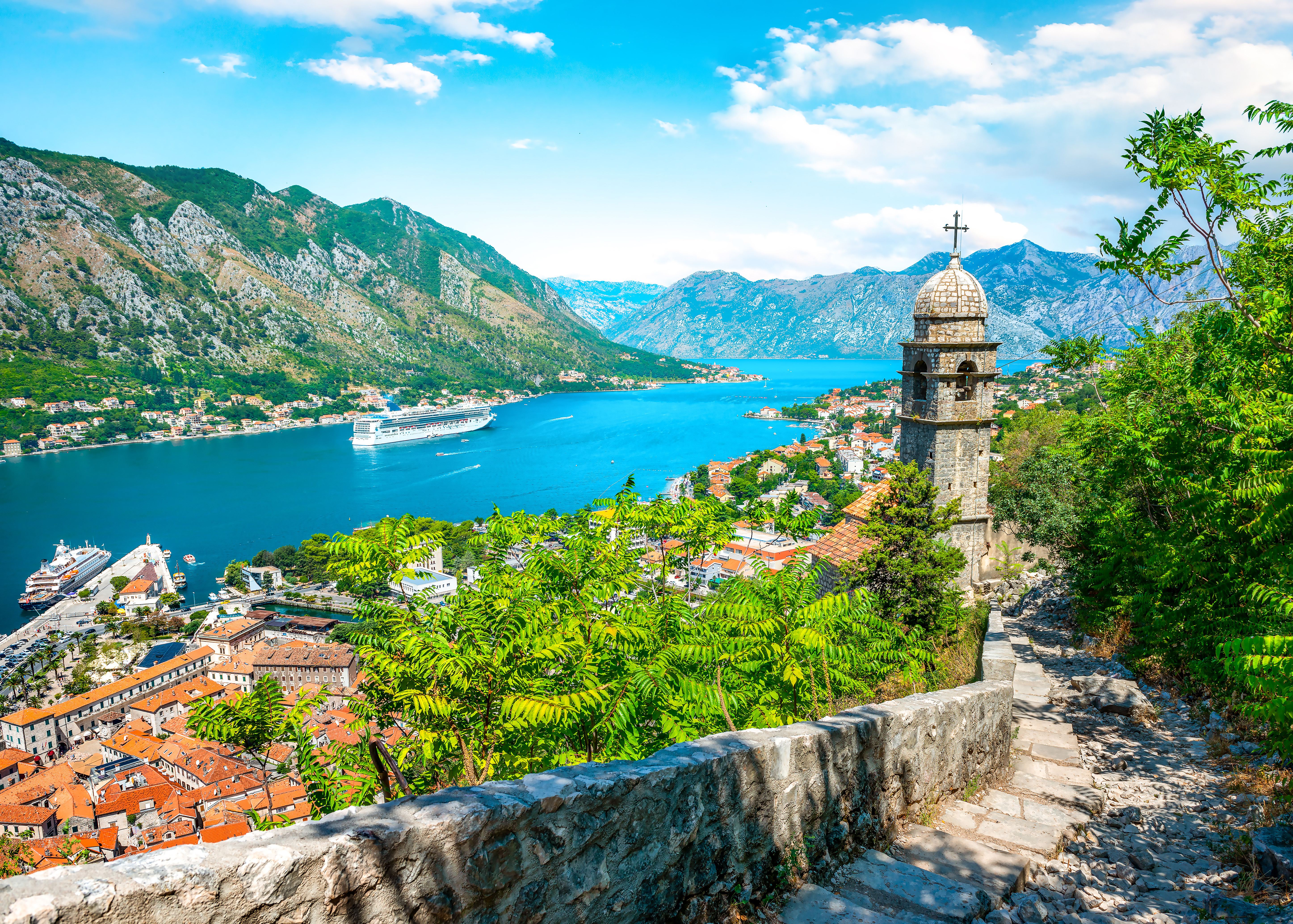 Kotor i Montenegro set fra bymuren med kirketårn, den gamle bys røde tage, turkisblåt hav og bjerge i baggrunden
