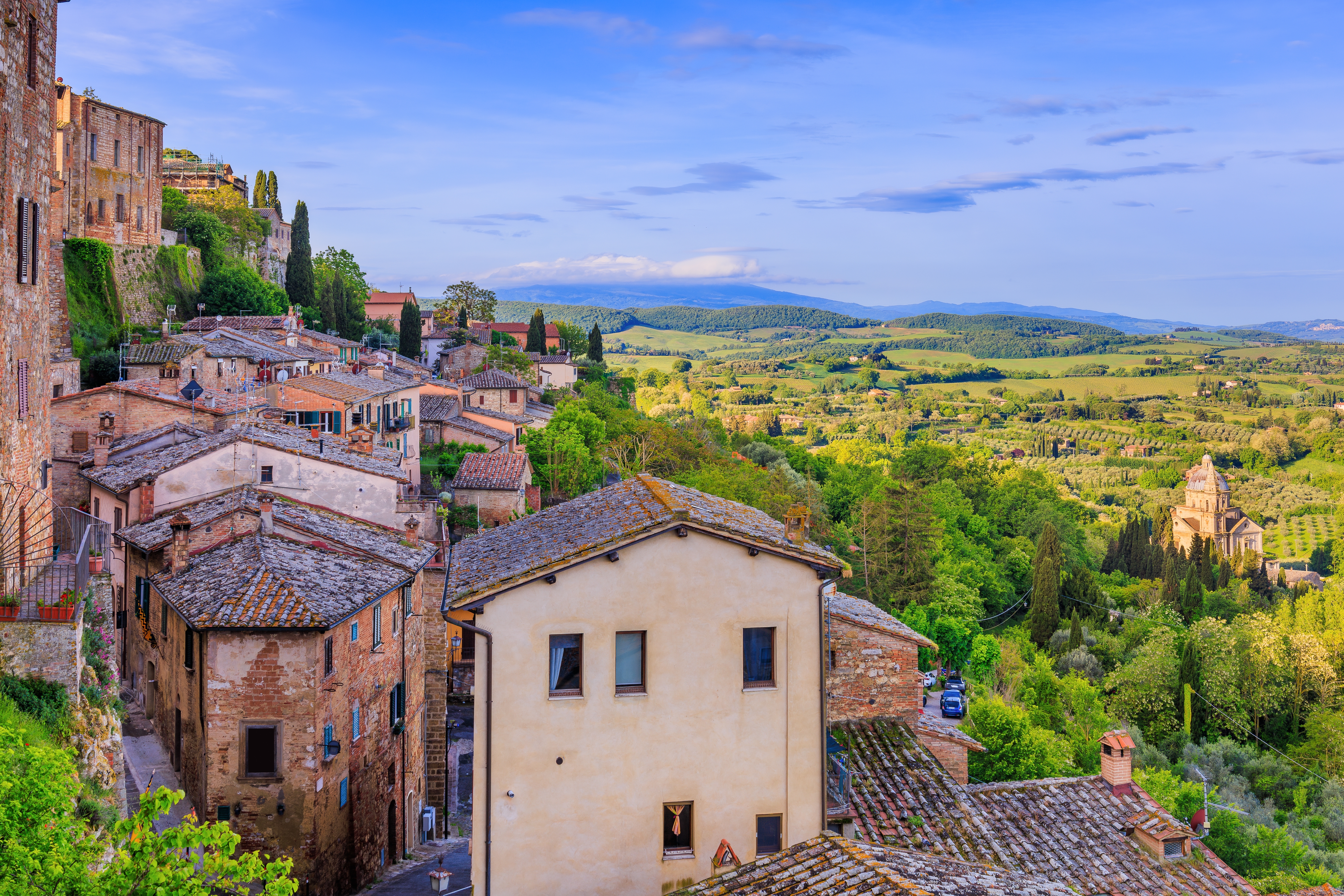 Idyllisk udsigt fra Montepulcianos gamle bydel over det toscanske landskab med grønne bakker, olivenlunde og historiske bygninger i Siena-provinsen