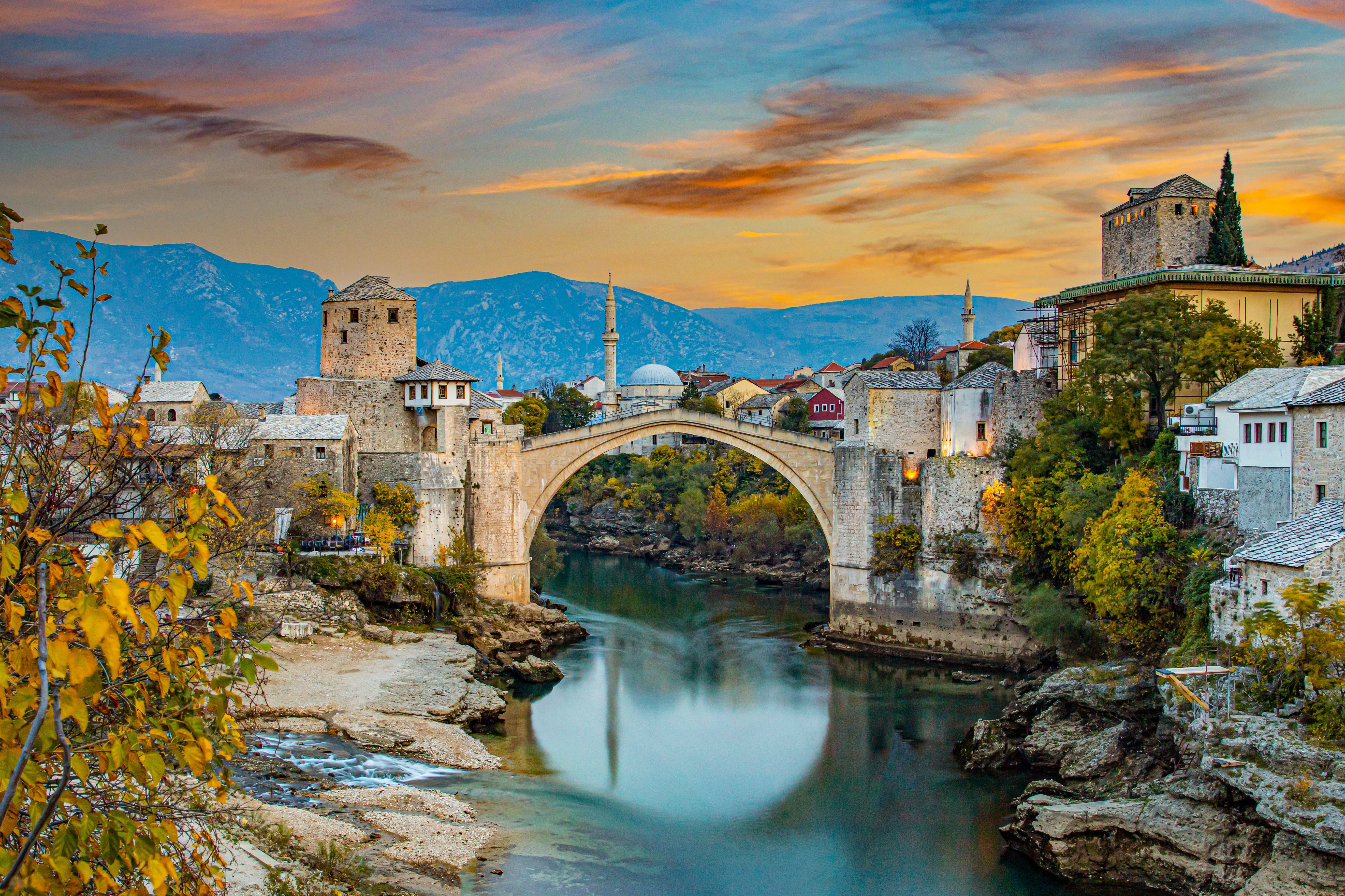 Den berømte bro i Mostar ved solnedgang med dramatisk himmel, turkisblå Neretva-flod og traditionelle bygninger i Bosnien-Herzegovina