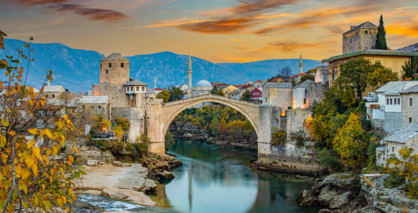 Den berømte bro i Mostar ved solnedgang med dramatisk himmel, turkisblå Neretva-flod og traditionelle bygninger i Bosnien-Herzegovina