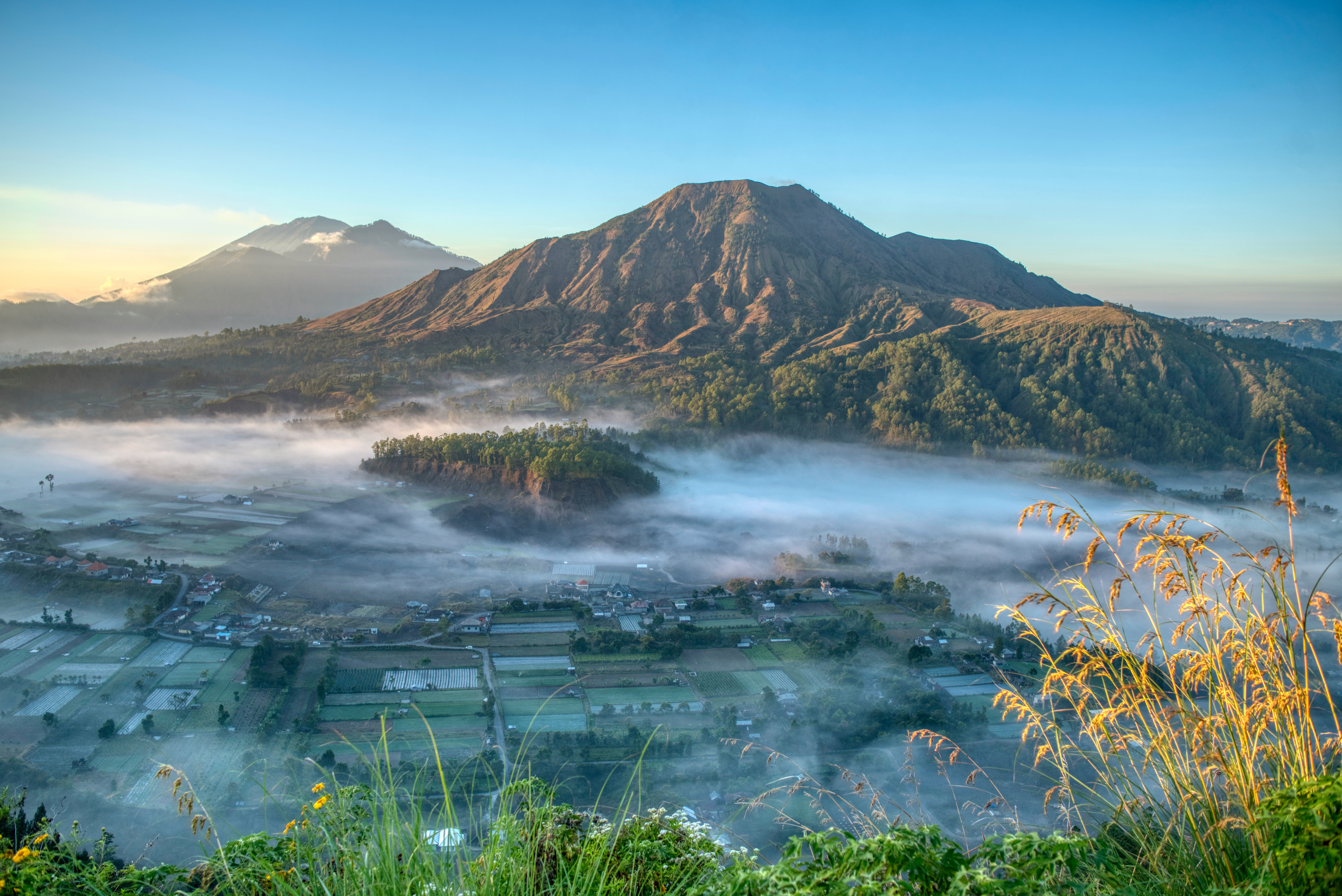 Majestætisk udsigt over Mount Batur vulkan med morgentåge over landsby og marker i Bali