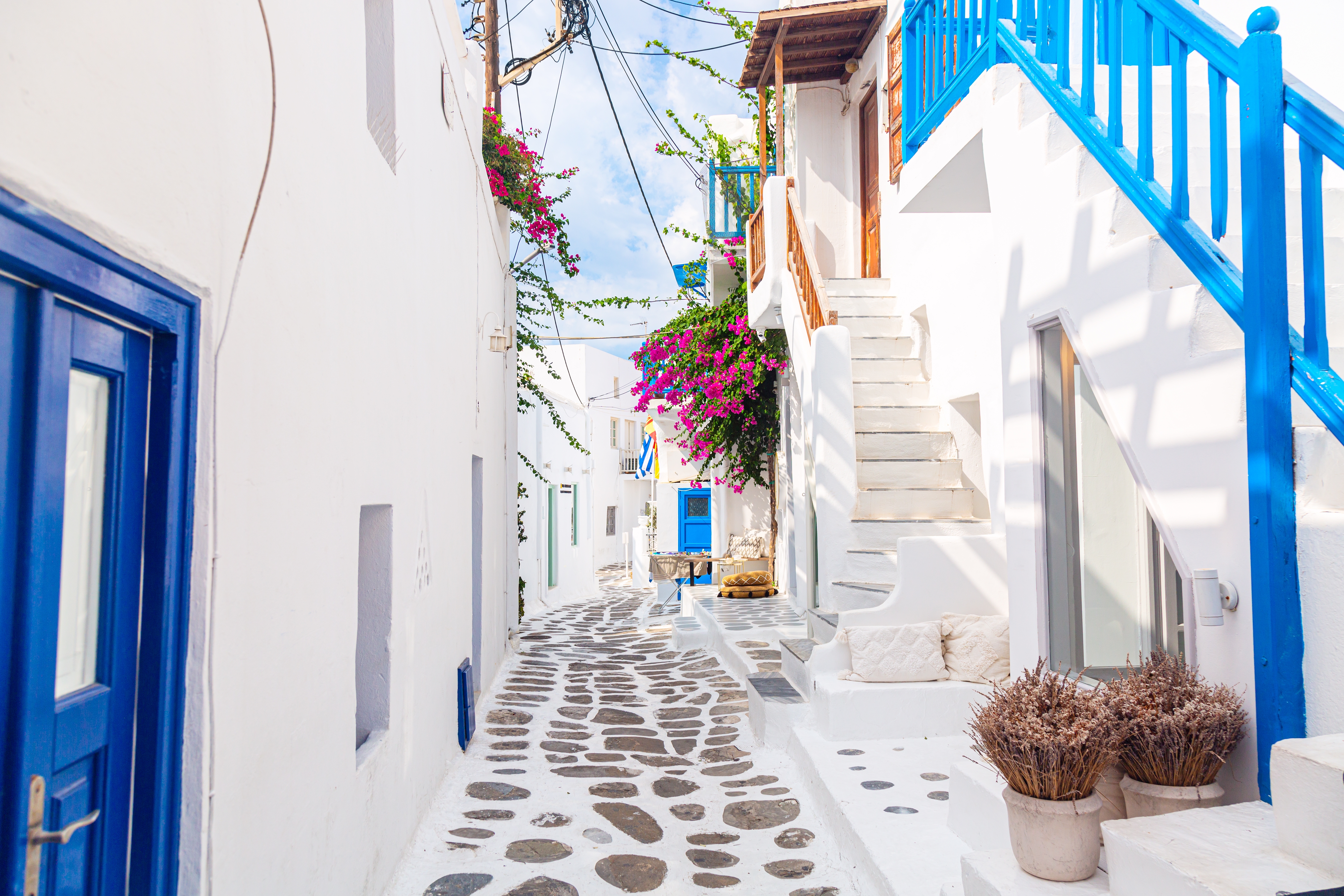 Pittoresk smal gade i Mykonos med hvidkalkede mure, blå detaljer og blomster, typisk for den græske ø-arkitektur