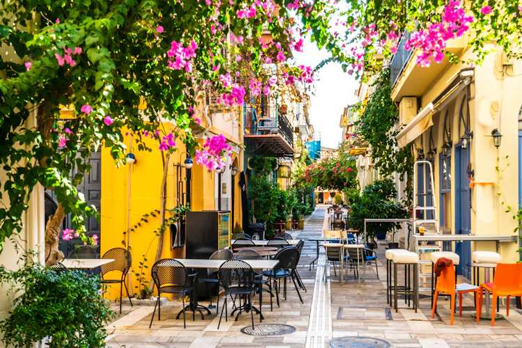 Stemningsfuld gade i den historiske by Nafplio i Grækenland med velbevarede stenhuse, karakteristiske blå skodder og en snæver stengade, der fører op til byens gamle tårn