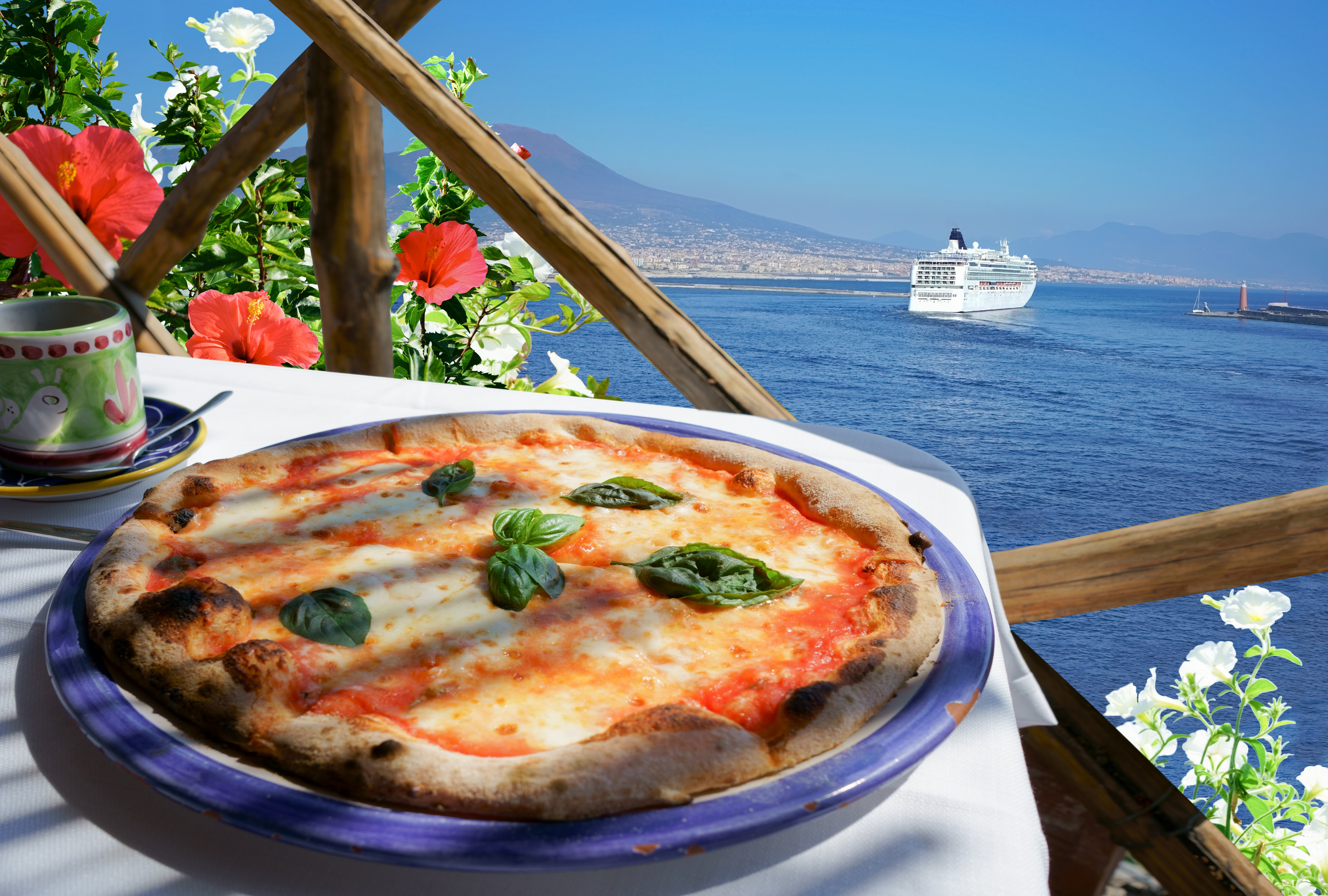 Lækker hjemmelavet pizza Margherita med tomat, mozzarella og basilikum på solrig terrasse med udsigt over Middelhavet og Vesuvius ved Napoli