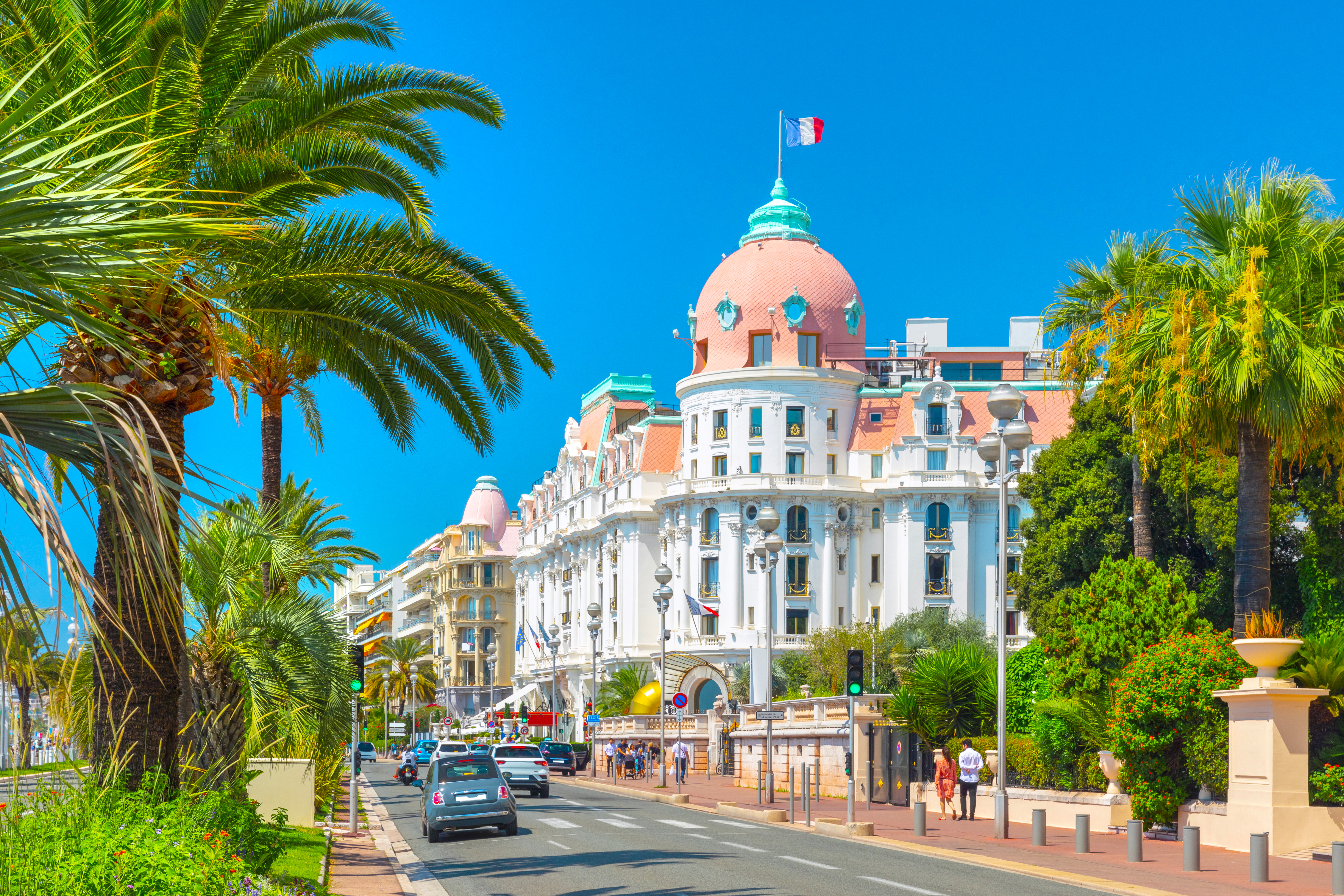 Solrig dag på Promenade des Anglais i Nice med det ikoniske lyserøde Hotel Negresco og høje palmer langs den berømte boulevard