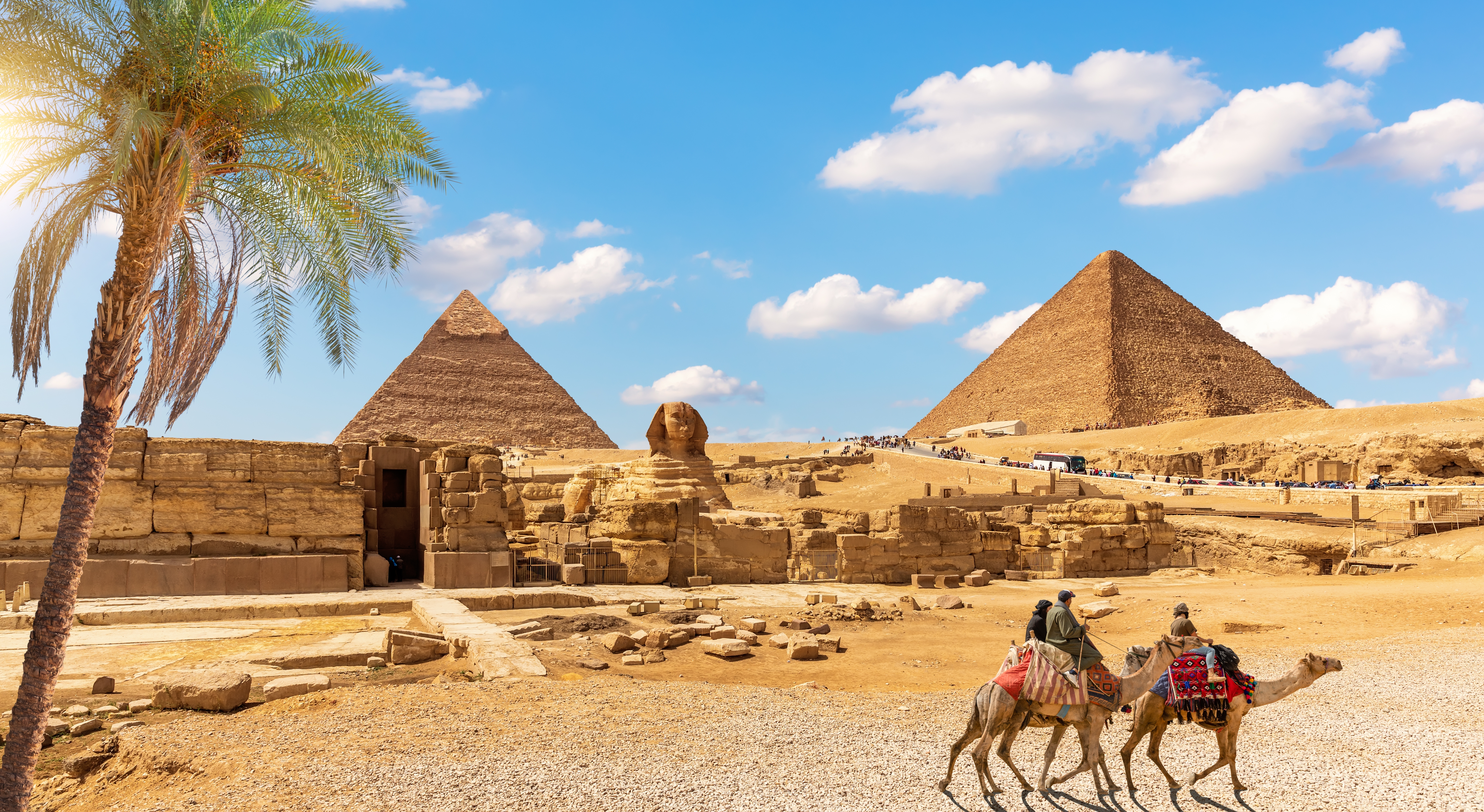 De berømte pyramider og Sphinx i Giza med kamelryttere og palmer under en blå himmel i Egypten
