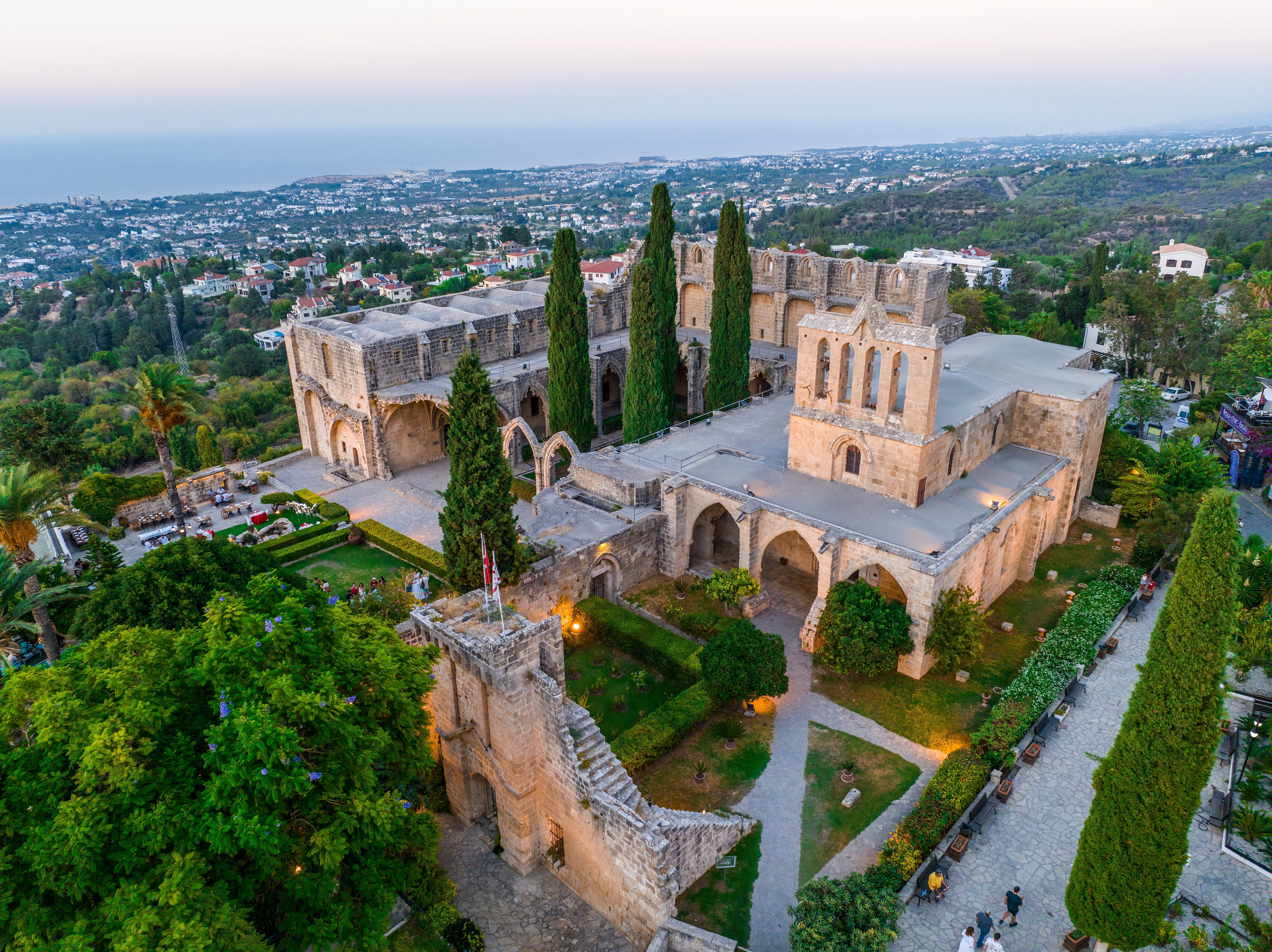 Panoramaudsigt fra luften over Bellapais Abbeys gotiske middelalderruiner ved Kyrenia på Nordcypern, med cyprestræer og udsigt over Middelhavet ved solnedgang