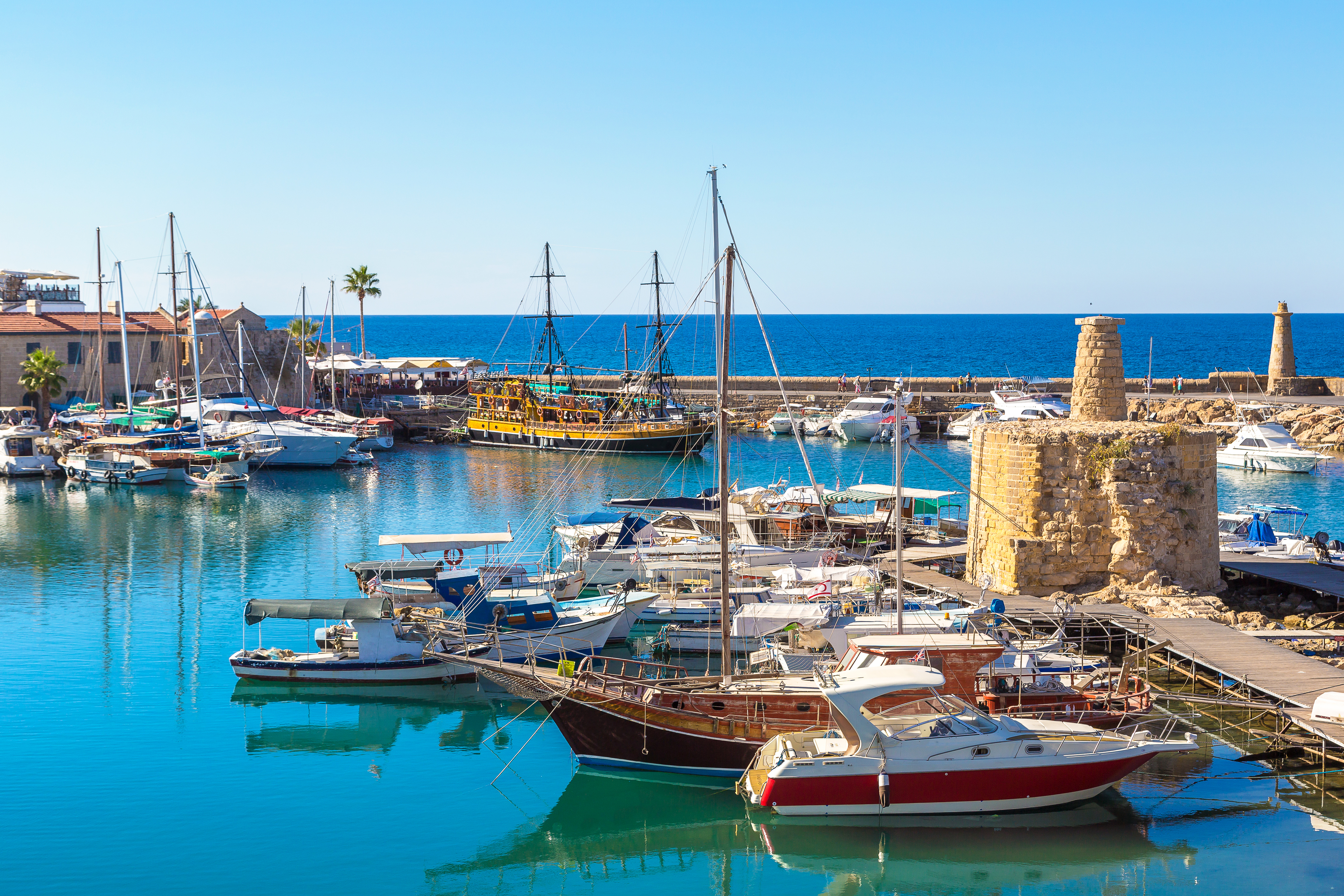 Smukt udsyn over den historiske marina i Kyrenia, Nordcypern, med farverige sejlbaade og lystbaade i det rolige turkisblaa middelhavsvand