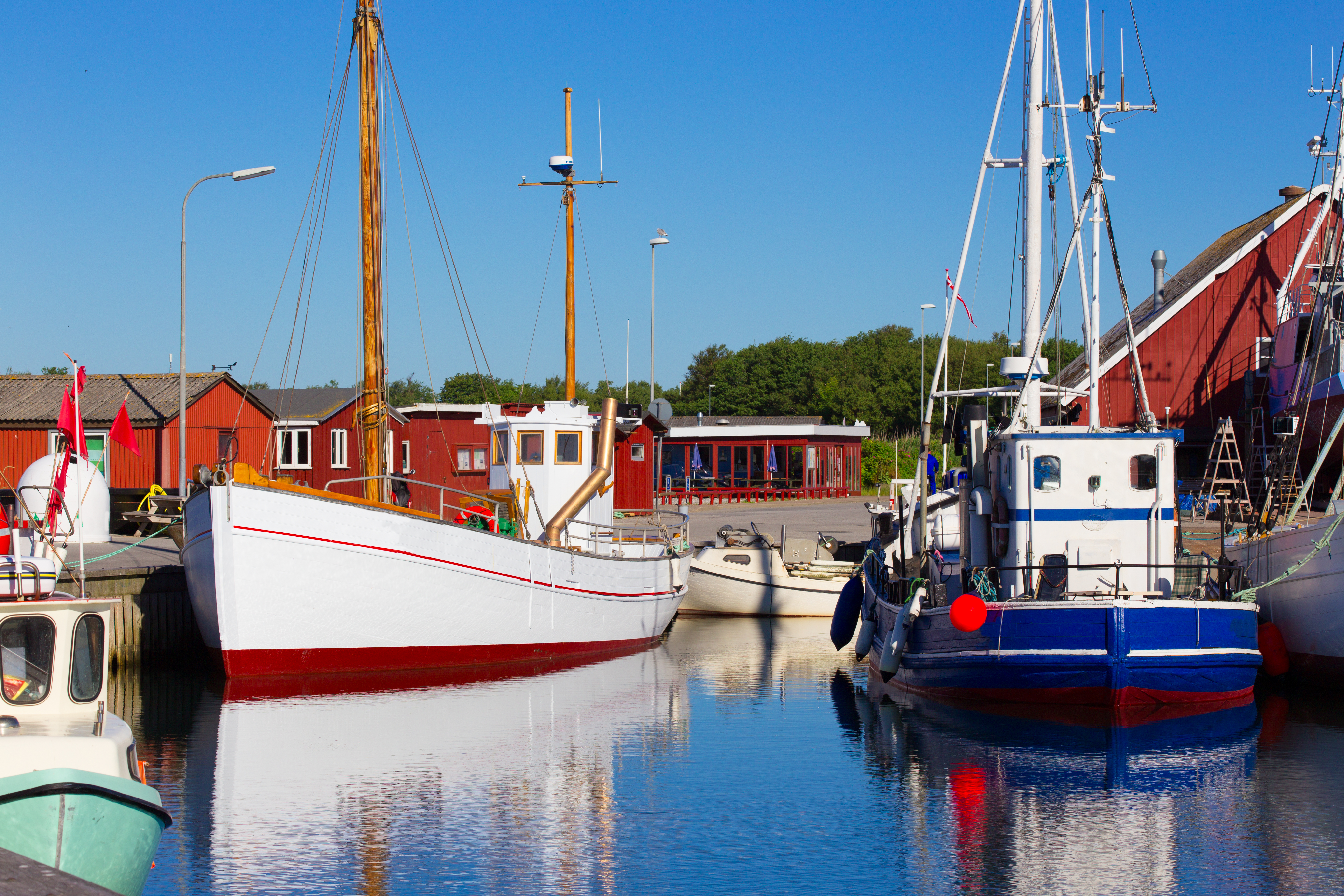 Malerisk nordisk fiskerihavn med hvide og blå både under blå himmel