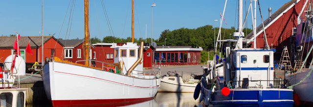 Malerisk nordisk fiskerihavn med hvide og blå både under blå himmel