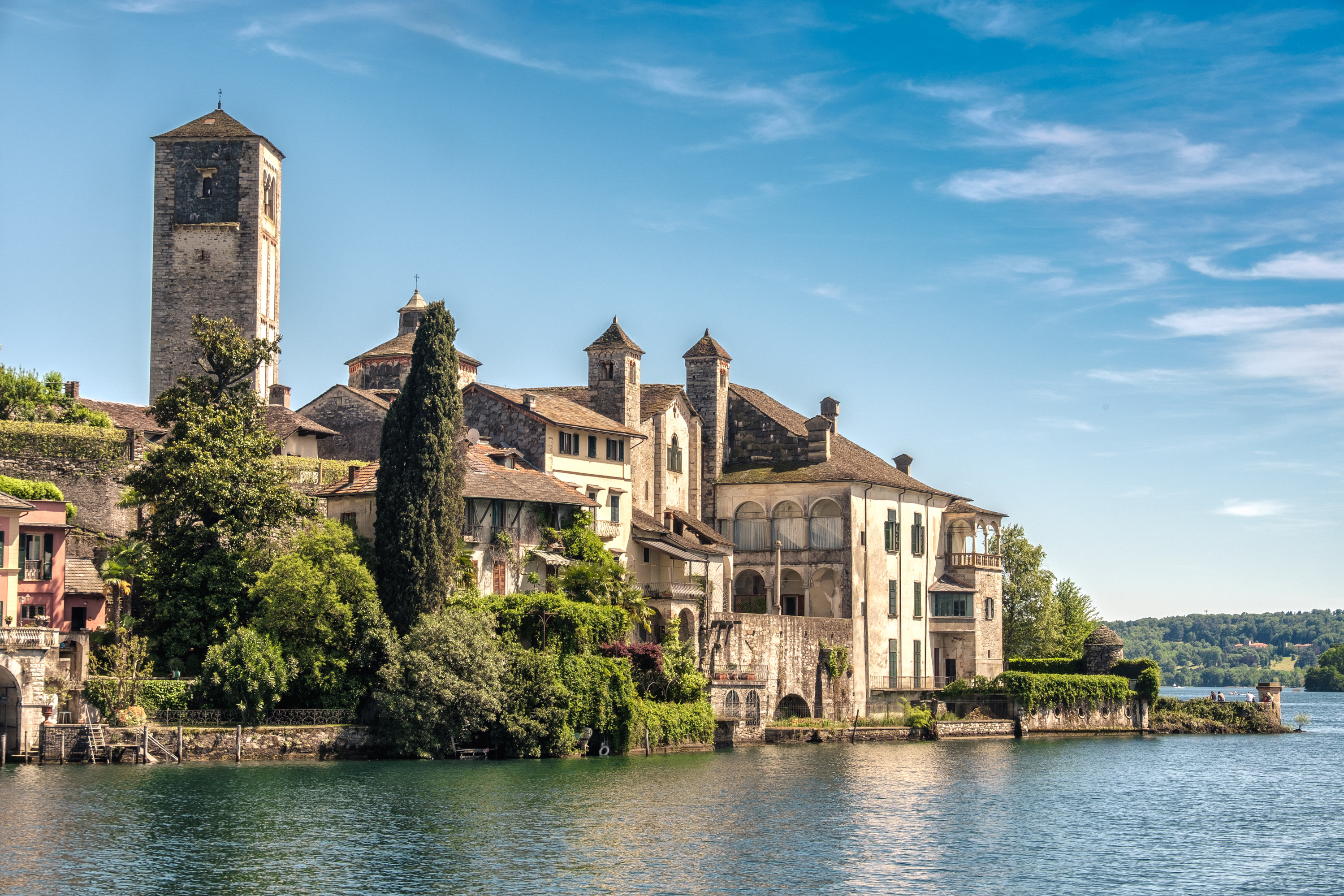 Charmerende San Giulio ø med middelalderlig arkitektur og cyprestrær spejlet i Orta-søens klare vand i Piemonte