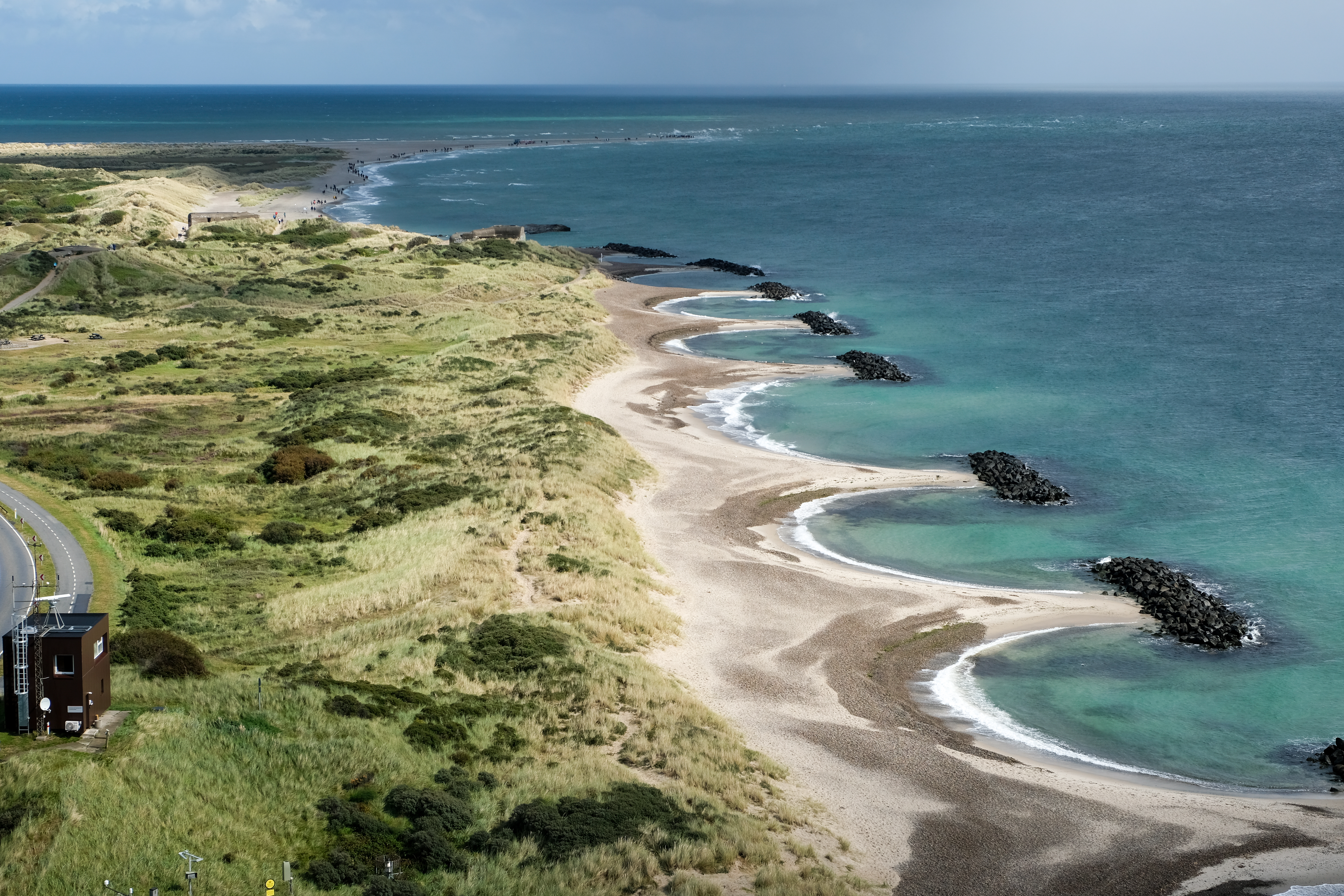 Udsigt over den naturskønne kyst ved Grenen nær Skagen i Nordjylland, med bølgende sandstrande og det blå hav på begge sider af Danmarks nordligste punkt