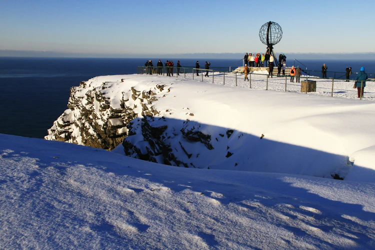 Eventyrligt vinterlandskab på Nordkap med snedækket plateau, den karakteristiske globus og besøgende der nyder den storslåede udsigt over havet