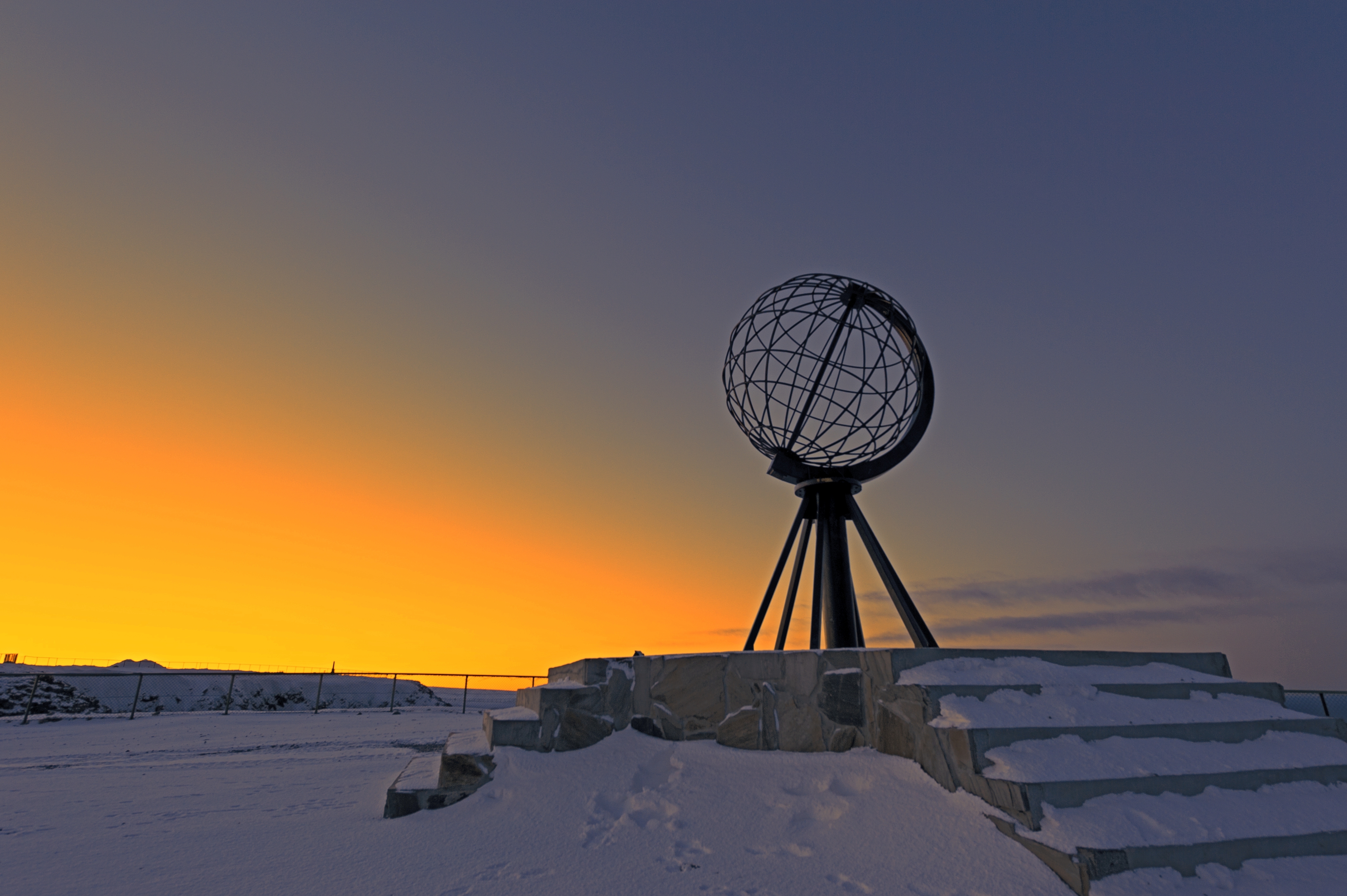 Det verdenskendte globusmonument på Nordkapp i Norge omgivet af sne og en flot gylden vinterhimmel ved solnedgang