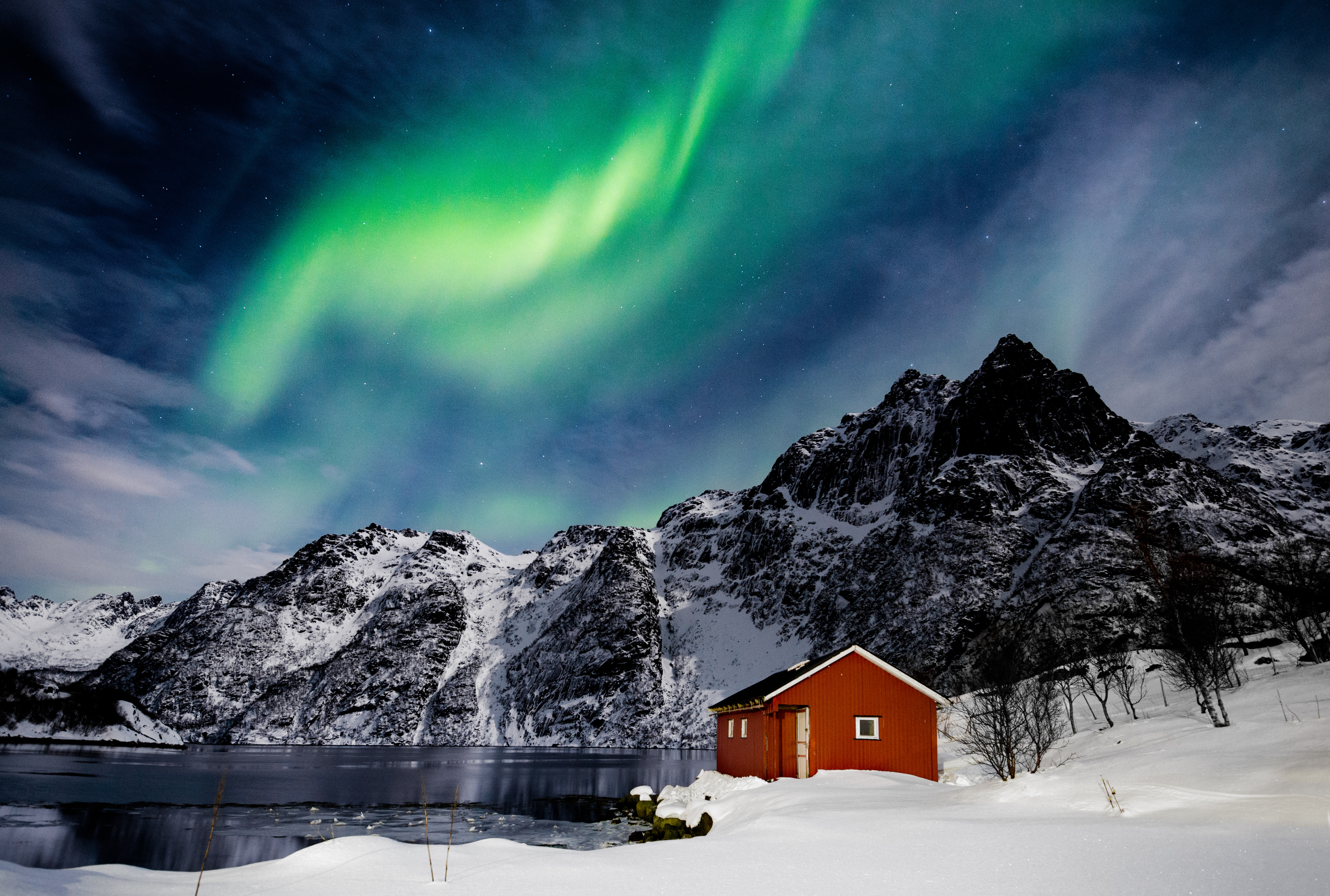 Fantastiske nordlys over klassisk rød rorbu ved frossen sø og snedækkede bjerge på Lofoten-øerne, Svolværs, Norge