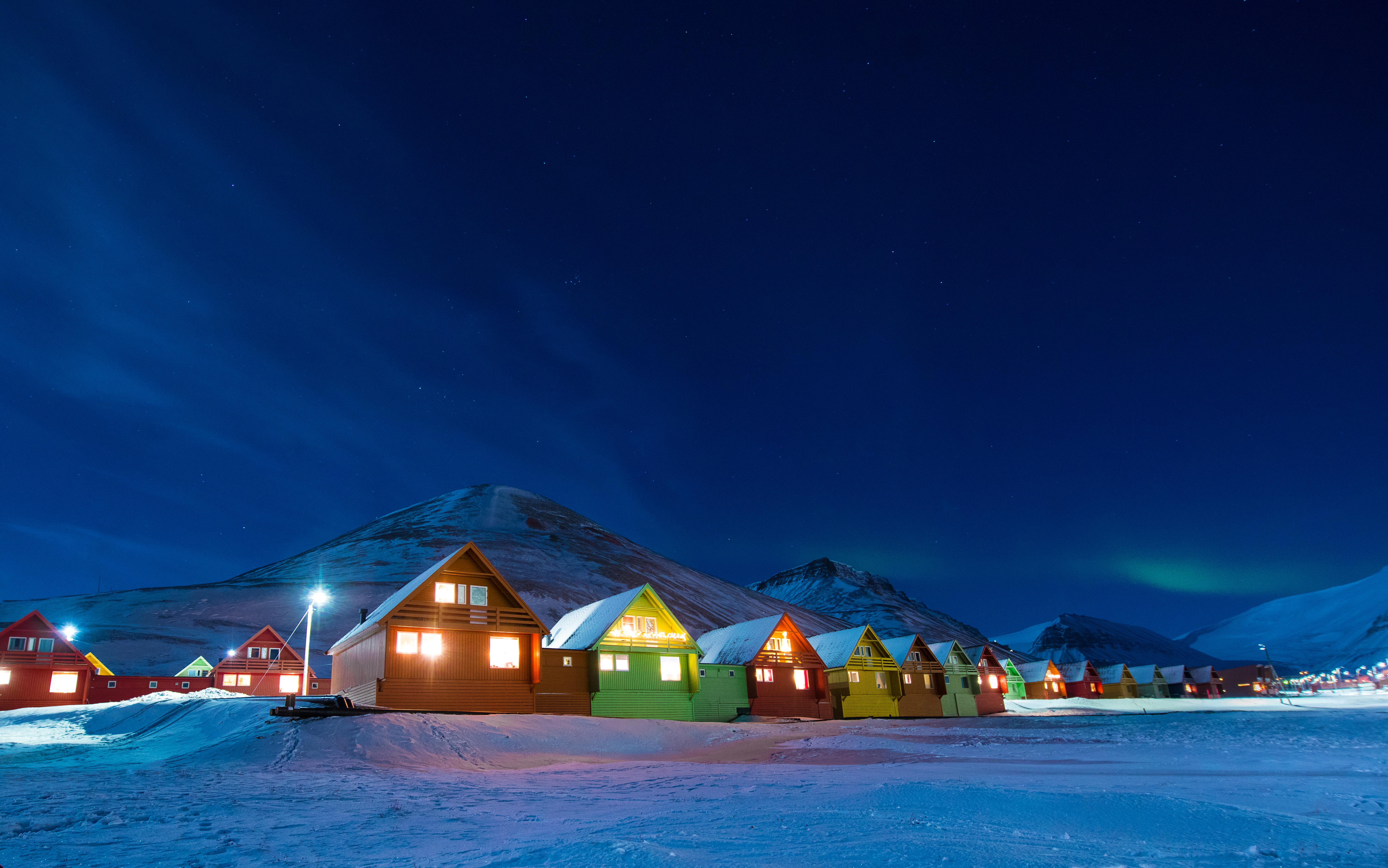 Spektakulært nordlys over farvestrålende hytter i sneen ved Longyearbyen på Svalbard i den arktiske nat