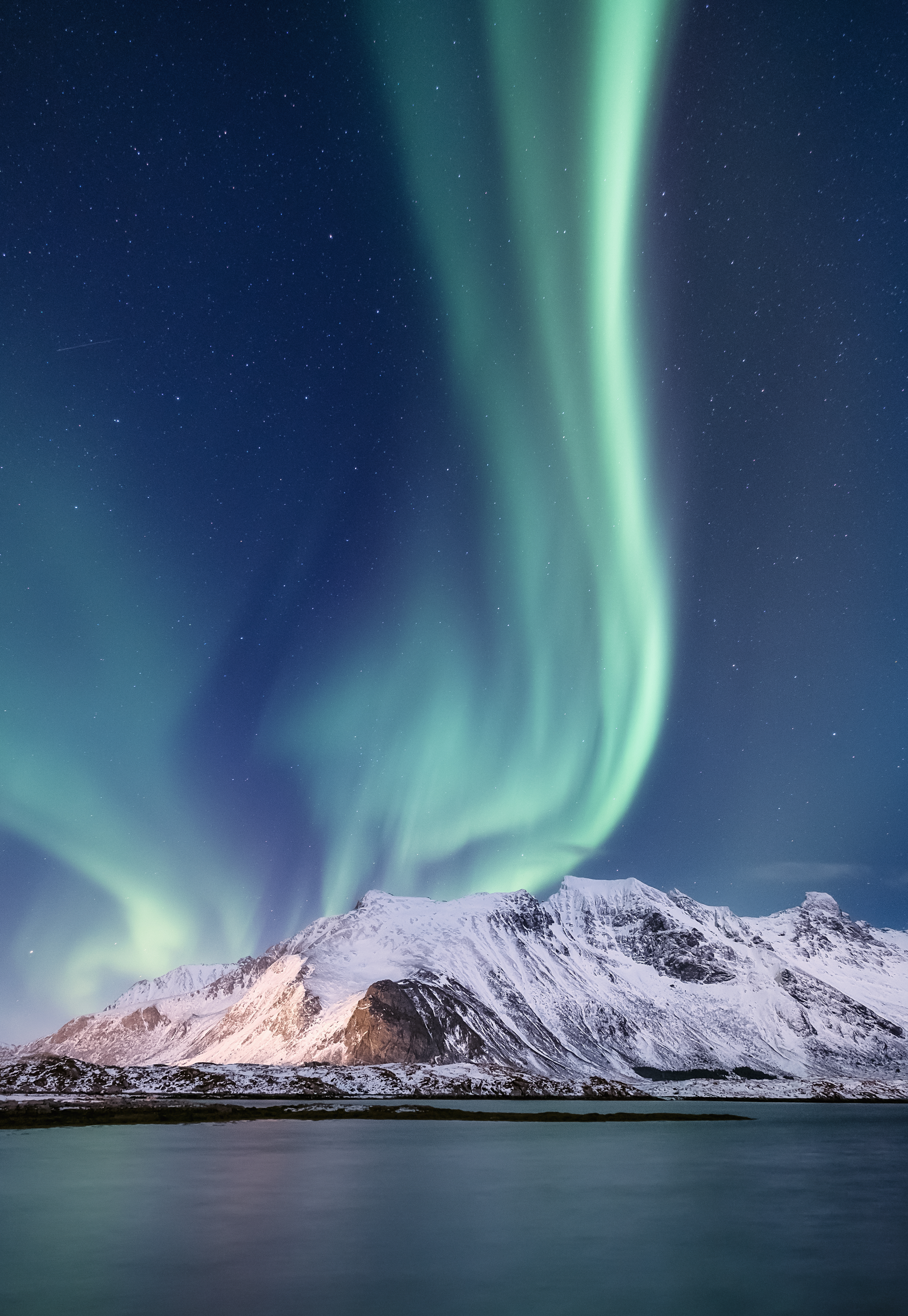 Fantastisk nordlys over snedækte fjelde og spejlblankt vand i Norge