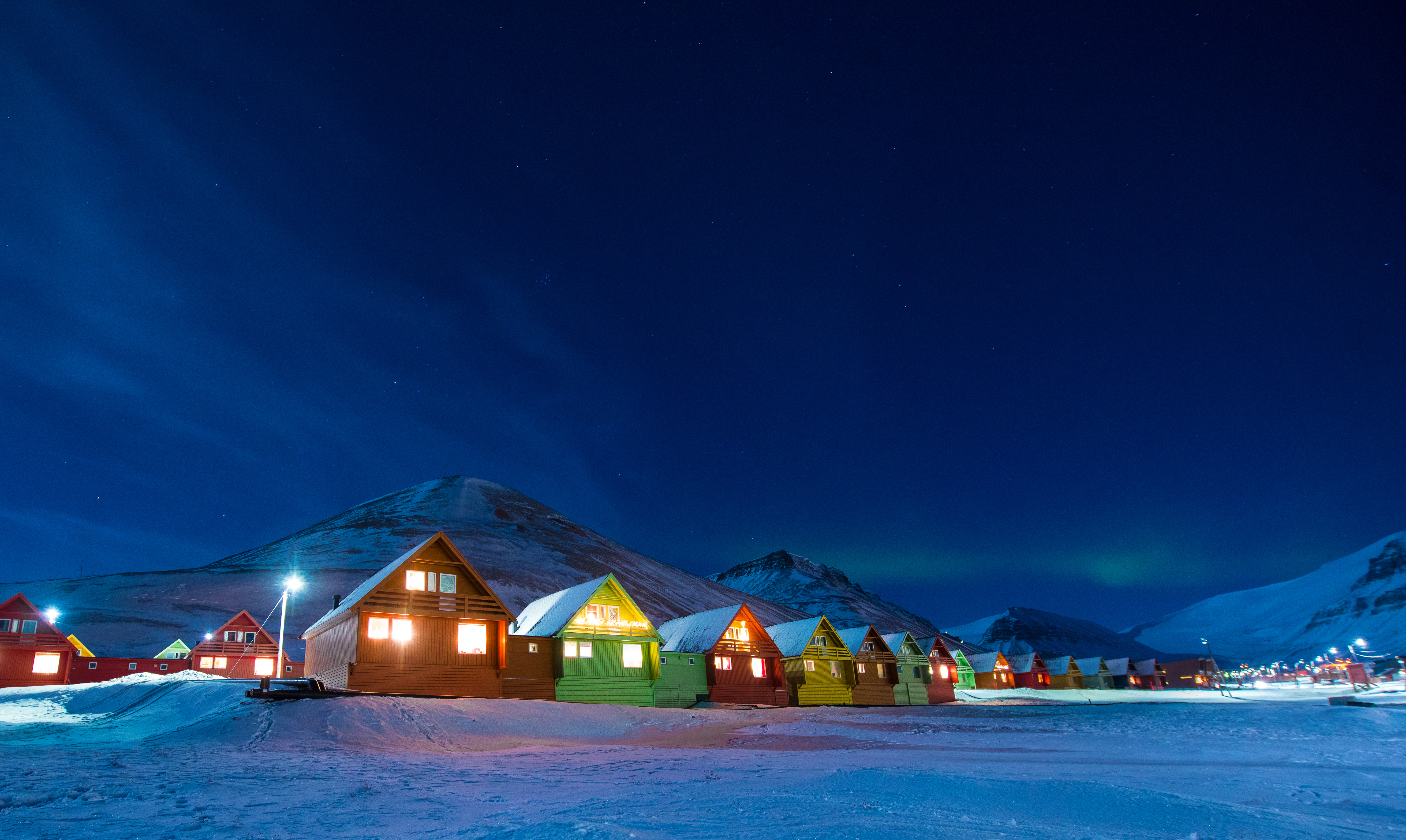 Nordlys over de ikoniske farverige huse i Longyearbyen på Svalbard med snedækkede bjerge og klar stjernehimmel