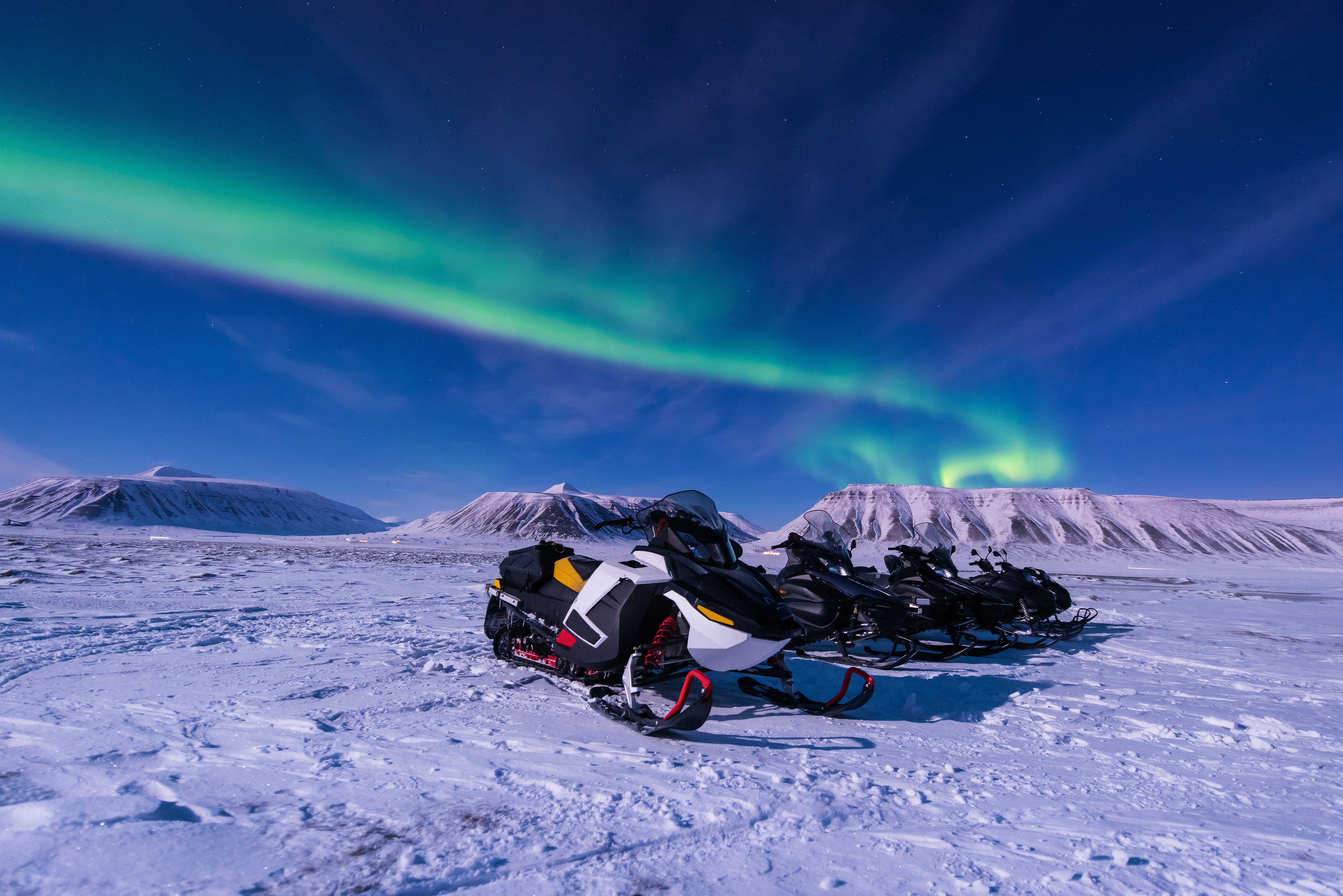 Nordlys danser hen over himlen mens snescootere holder parkeret i vinterlandskabet ved Longyearbyen på Svalbard