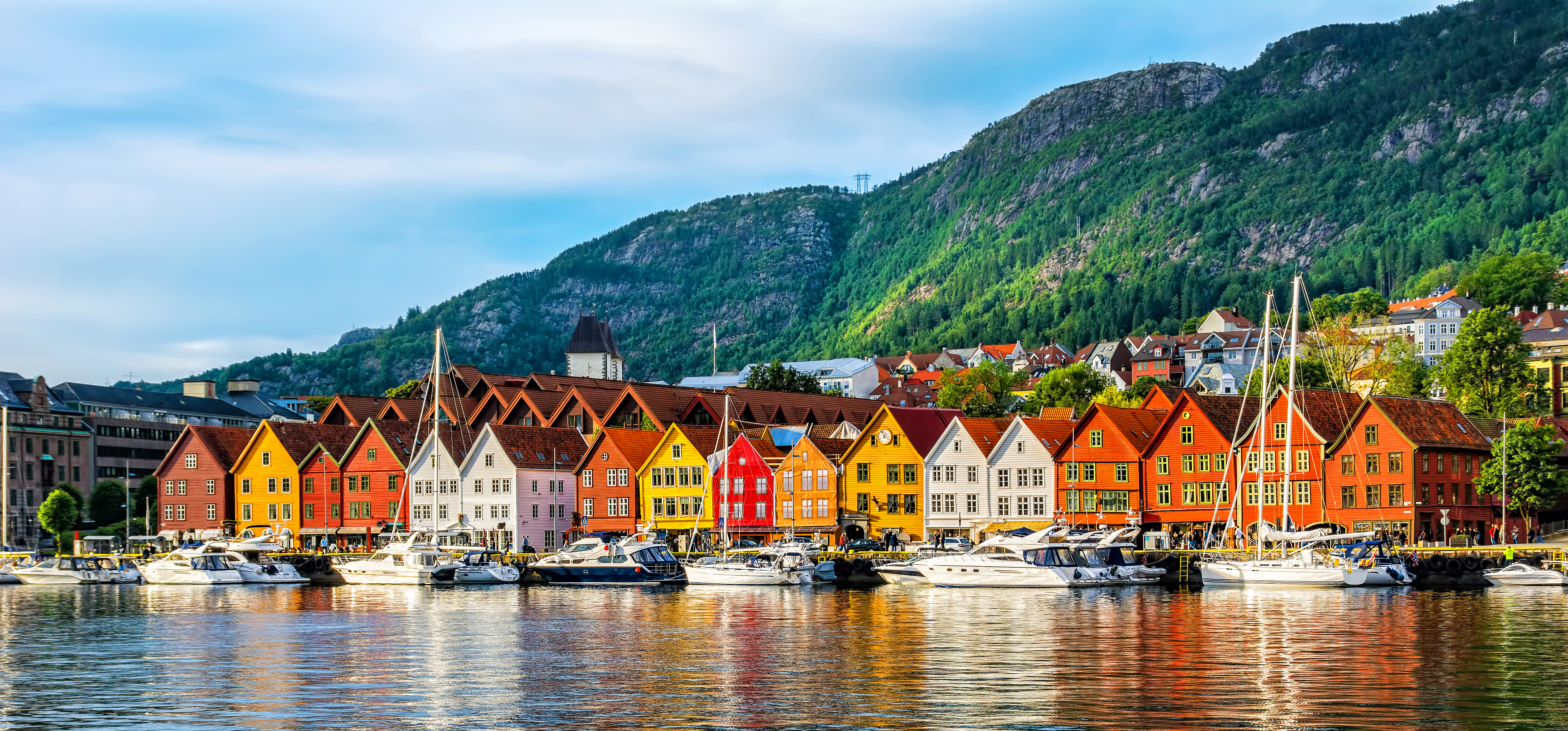 Smukke træhuse i forskellige farver langs Bergen havn med norske bjerge i baggrunden