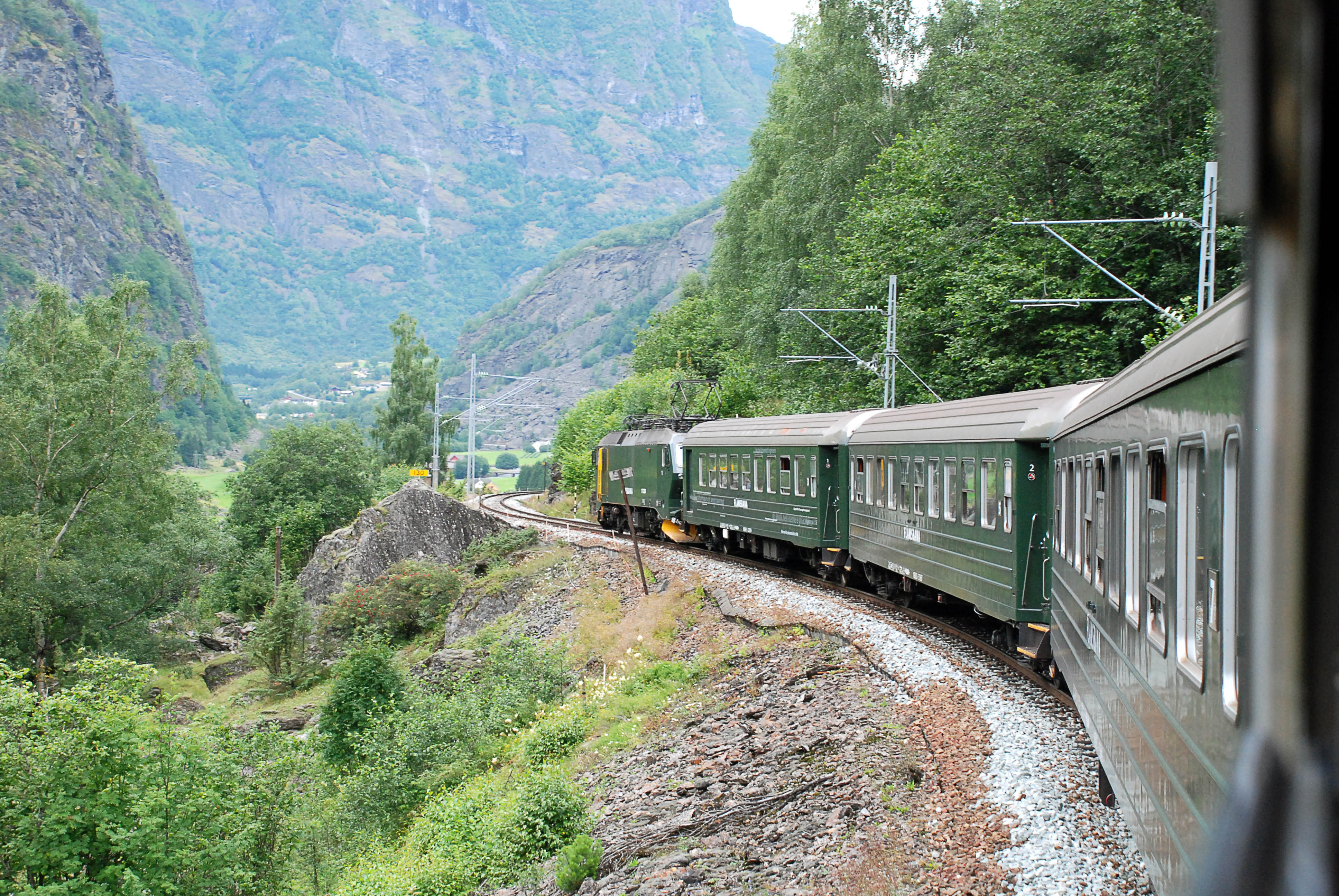 Norsk bjergbane med passagertog i smuk groen dal mellem hoeje bjergtinder om sommeren