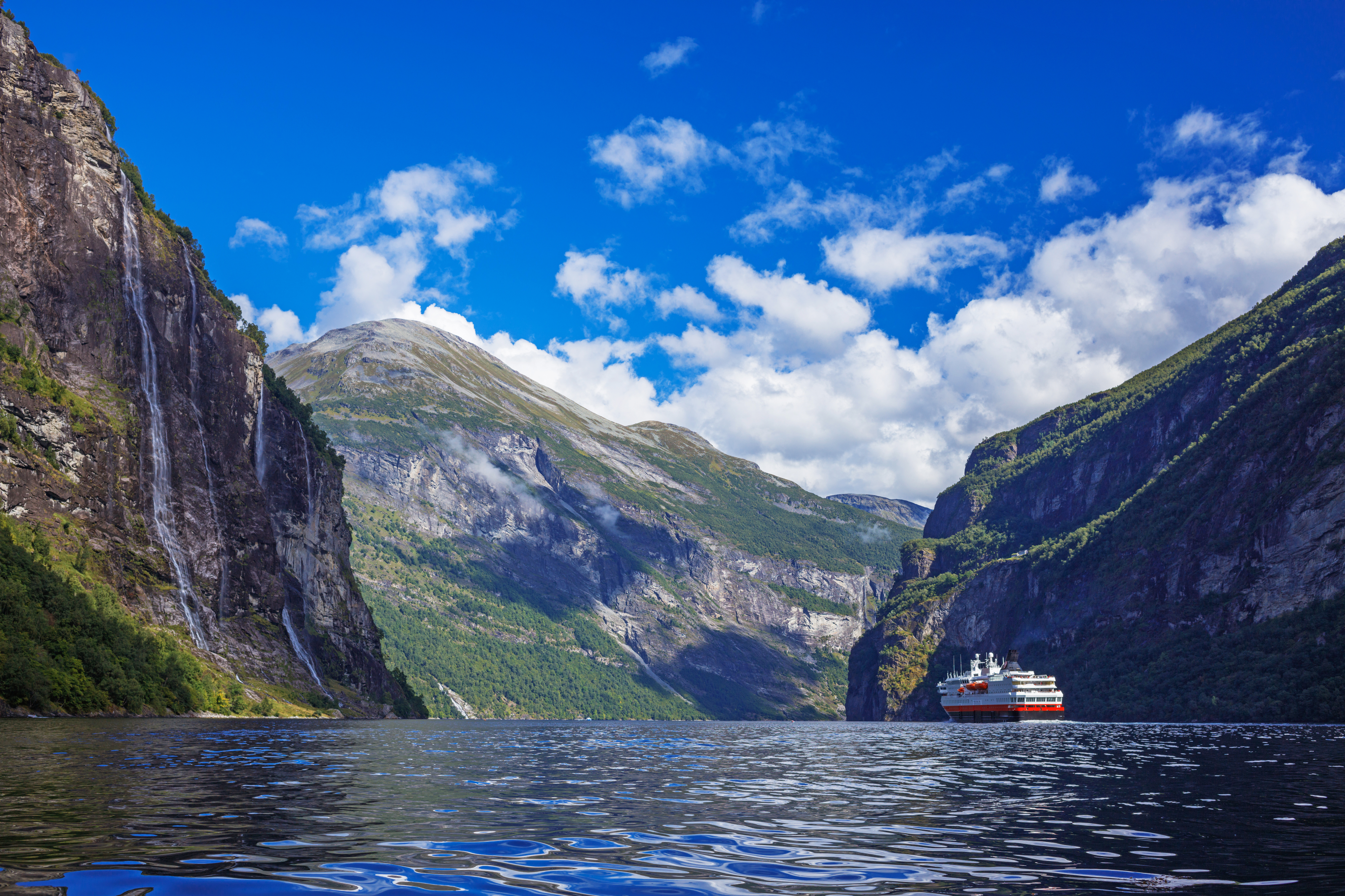 Skib på det naturskønne Geirangerfjord i Norge omgivet af dramatiske bjerge og smukke vandfald på en solrig sommerdag