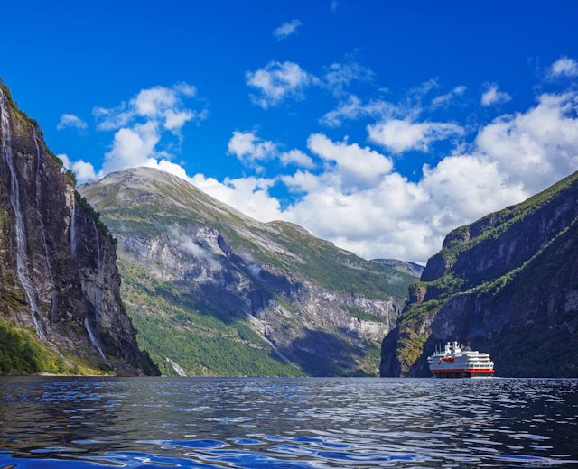 Skib på det naturskønne Geirangerfjord i Norge omgivet af dramatiske bjerge og smukke vandfald på en solrig sommerdag