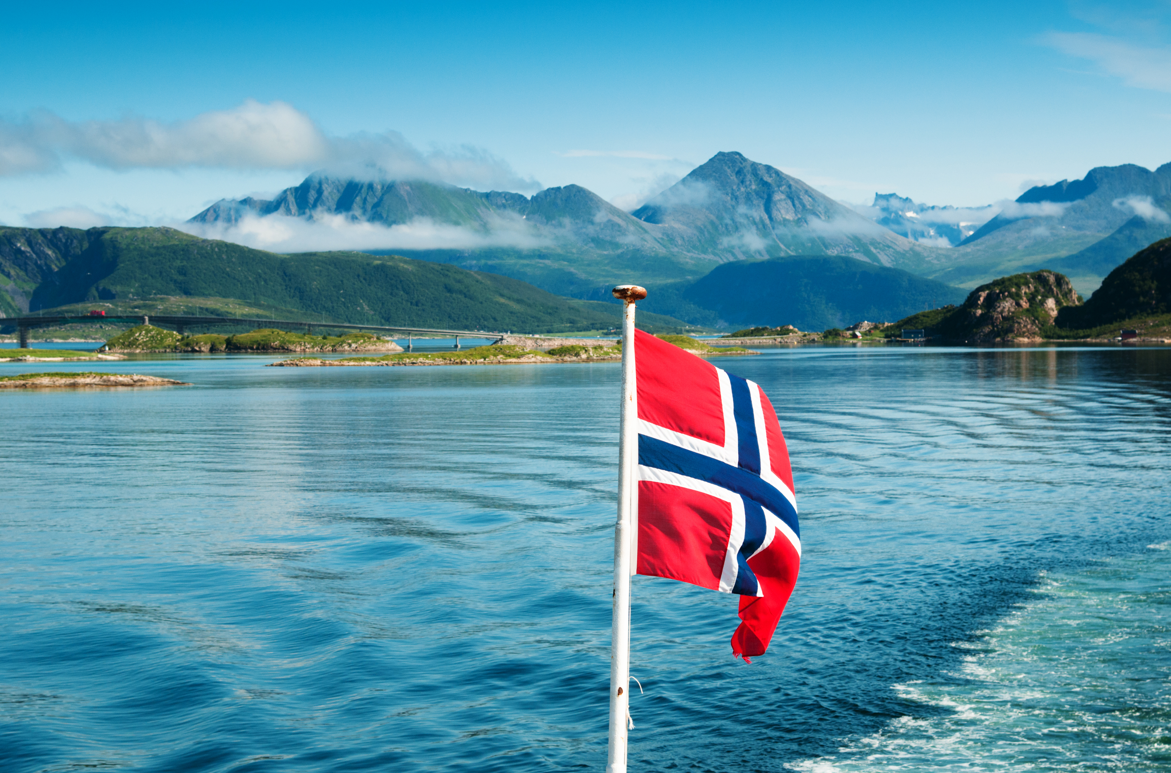 Norsk flag på en båd med smukt norsk fjordlandskab og grønne bjerge på Lofoten om sommeren
