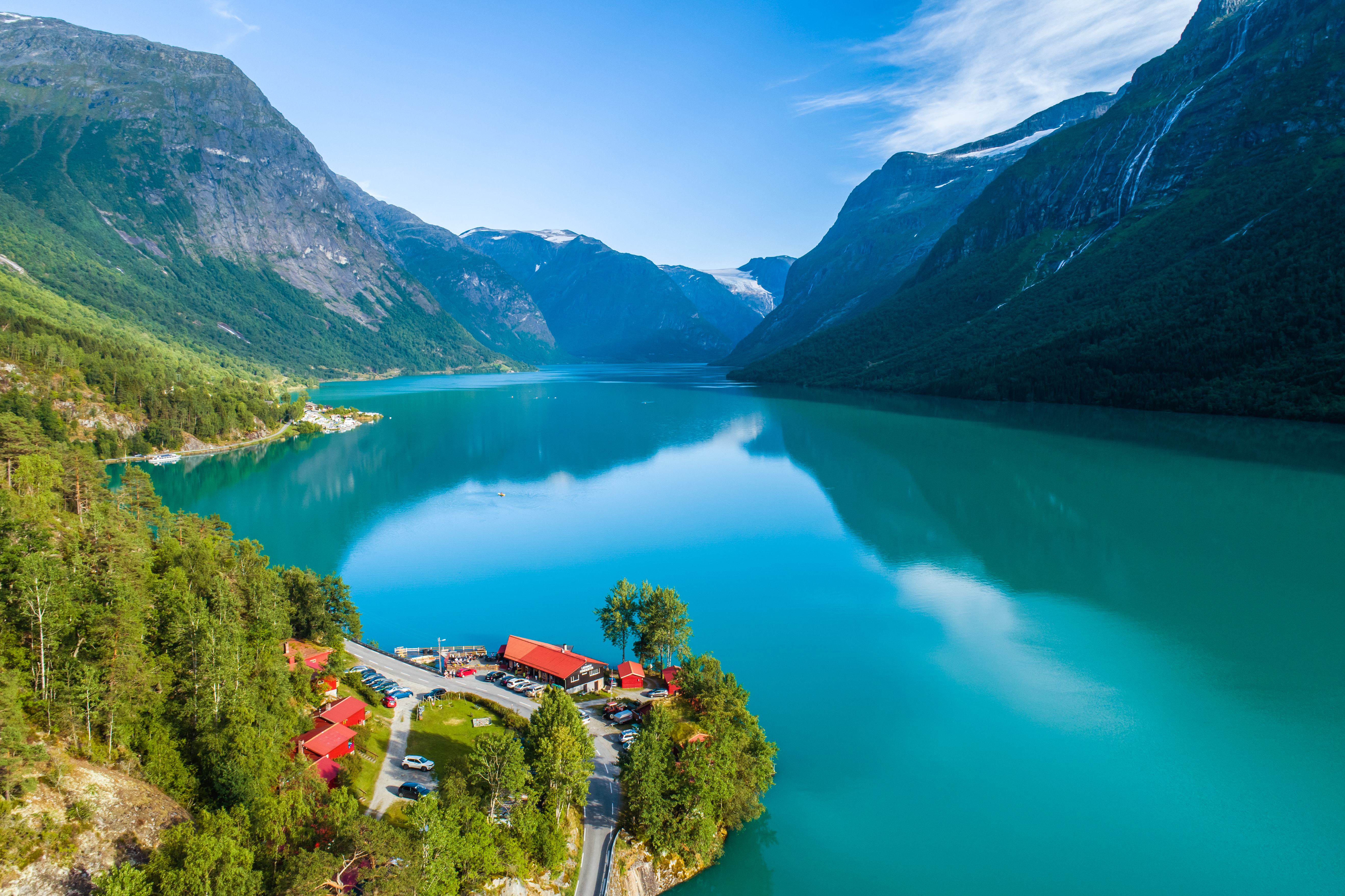 Imponerende luftfoto af Lovatnet i Norge med turkis vand, sneklædte bjerge og charmerende lille landsby