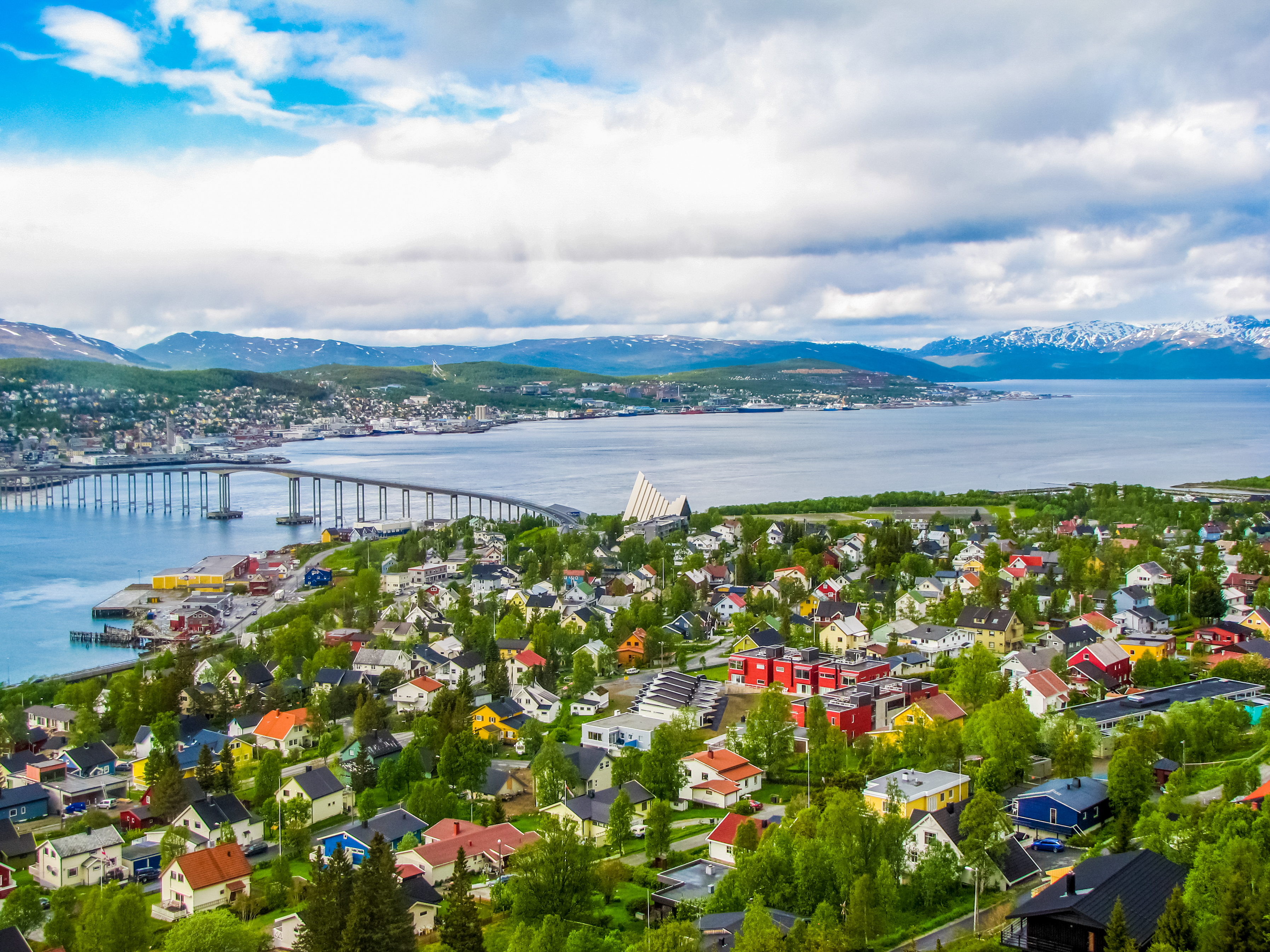 Malerisk udsigt over Tromsø i sommertiden, hvor byens farverige bygninger, den markante bro og havnen harmonerer med de omkringliggende fjorde og bjerge i det nordnorske landskab