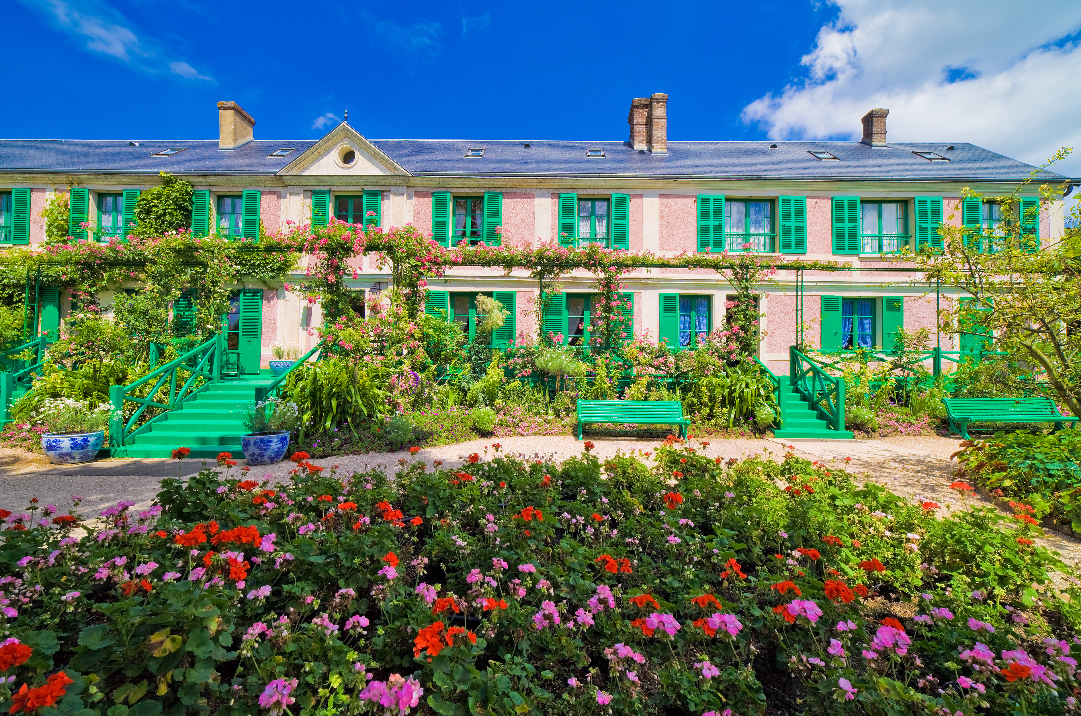 Den idylliske facade af Claude Monets hus i Giverny, Normandiet med de ikoniske grønne skodder omgivet af en frodig have med farverige geranier og roser