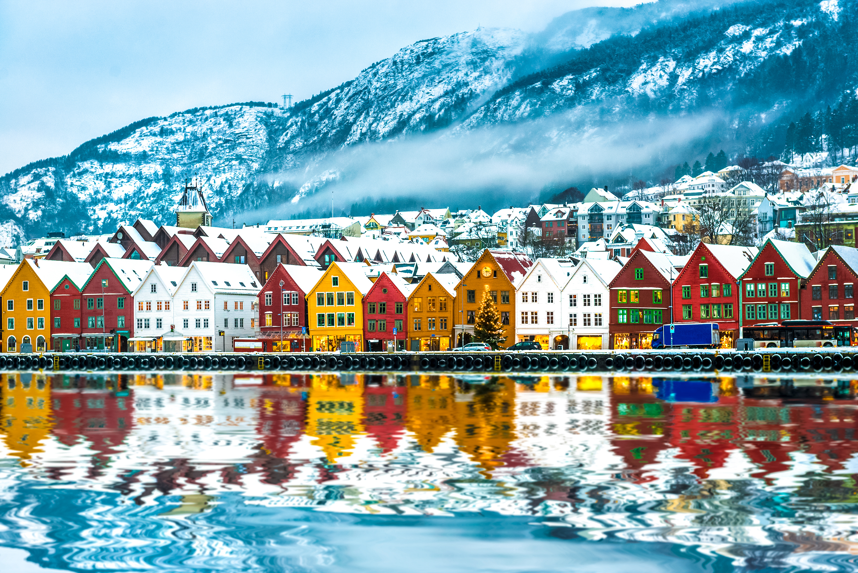 Norske træhuse ved Bergen havn med snedækte bjerge og refleksioner i vandet